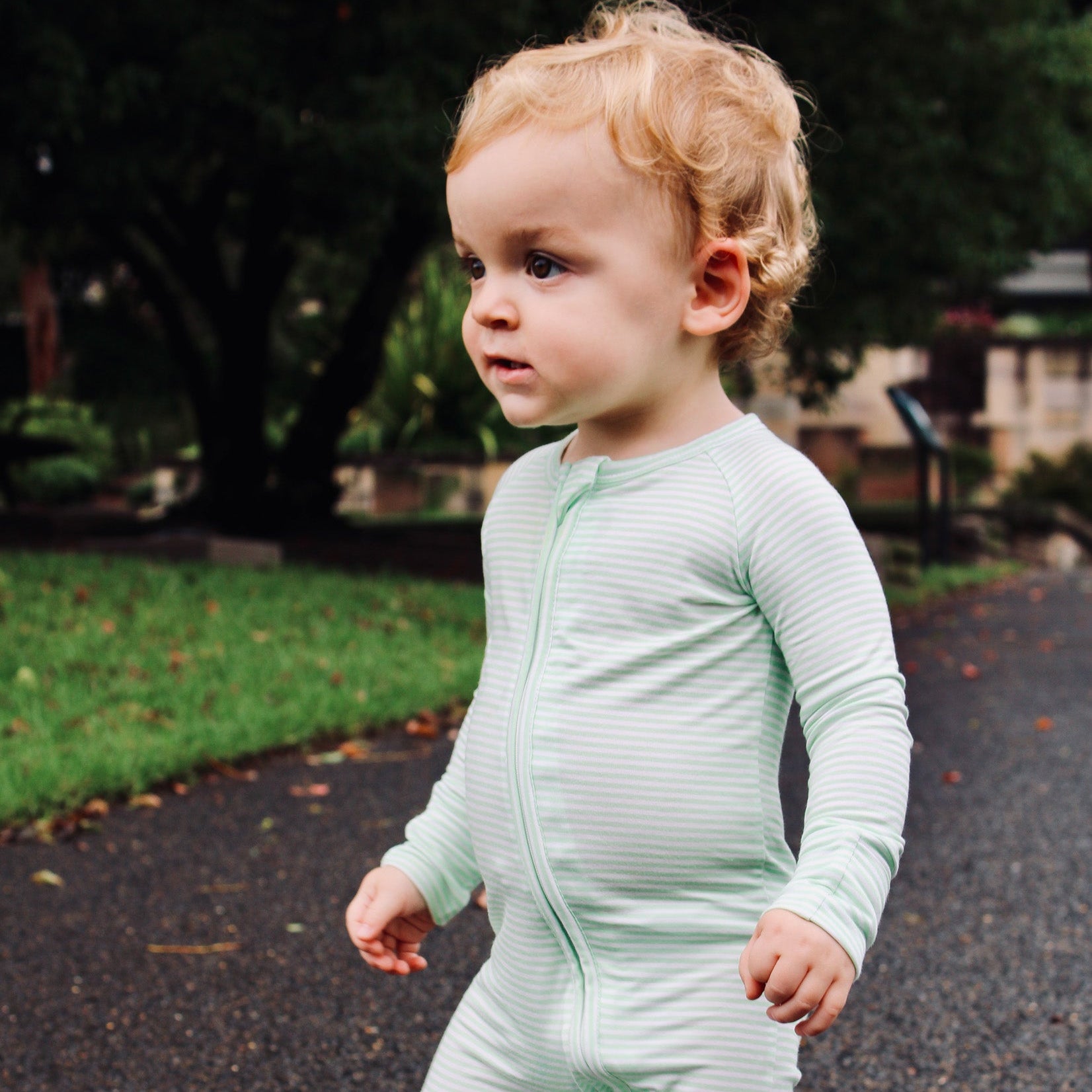 Baby boy wearing Motette green stripe bamboo sleeper with two-way zipper and fold-over foot cuffs