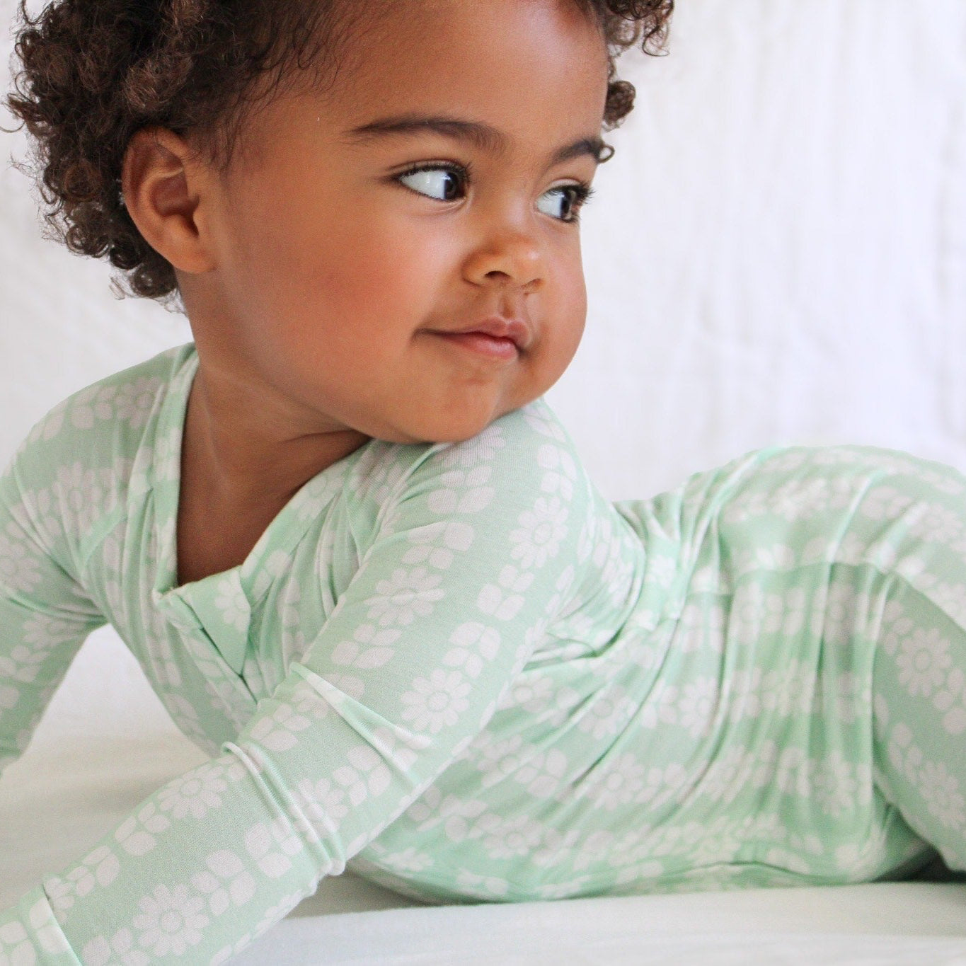 Baby girl wearing Motette Mint Meadows bamboo sleeper with two-way zipper and fold-over feet