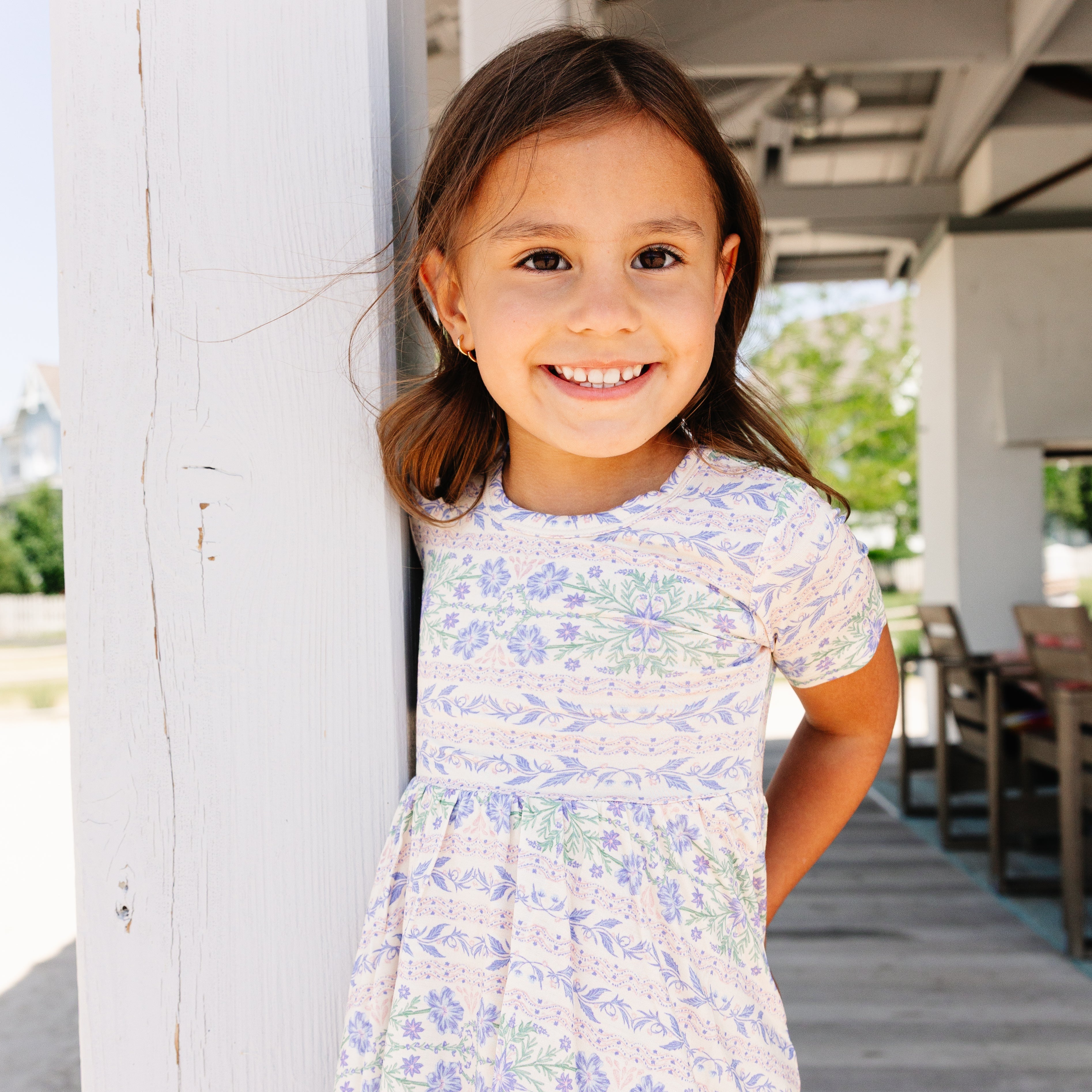 Young girl in a floral bamboo twirl dress standing on a wooden deck.