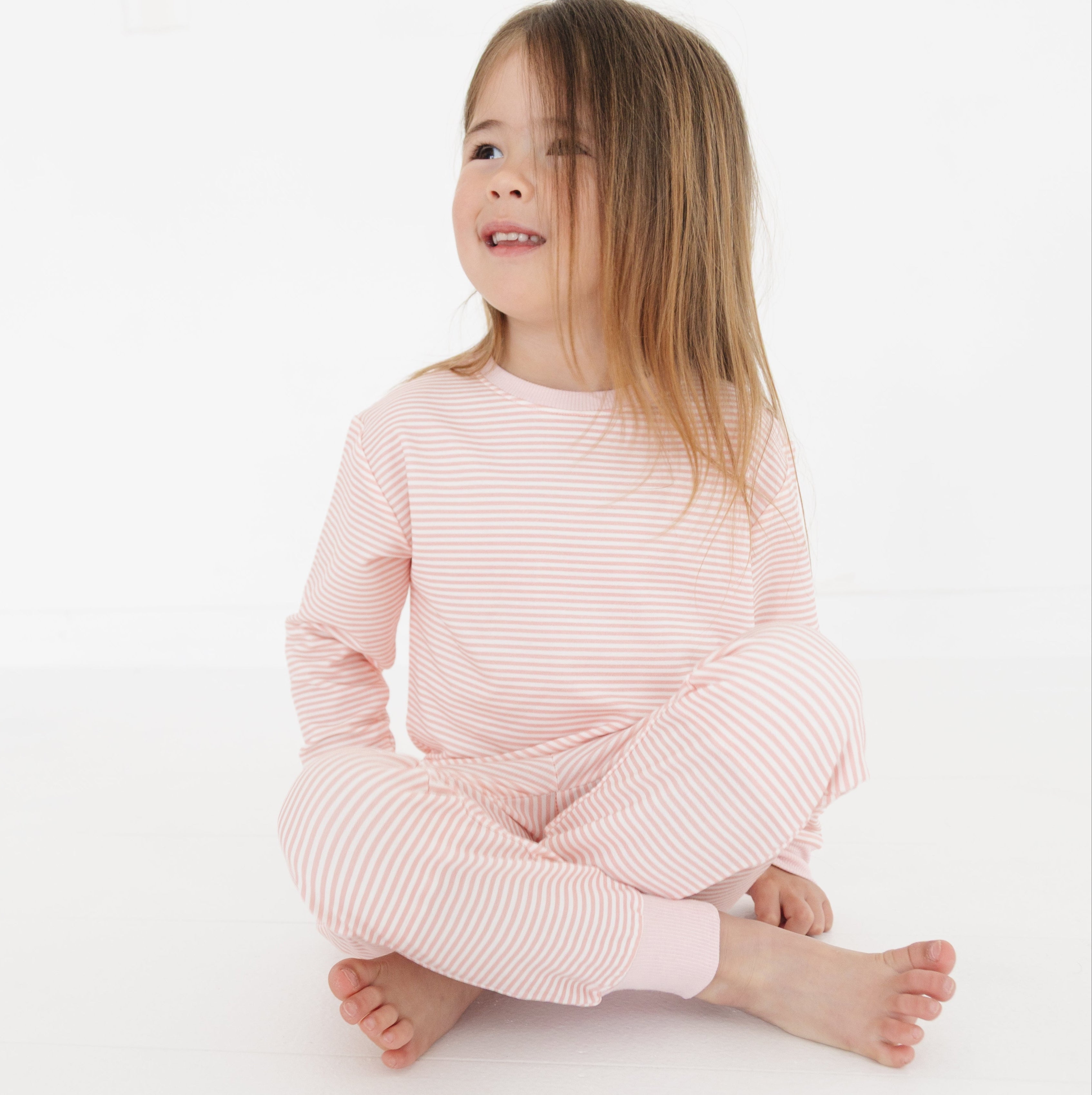 Girl sitting cross-legged in Motette’s pink bamboo lounger, smiling softly with sleeves pushed up