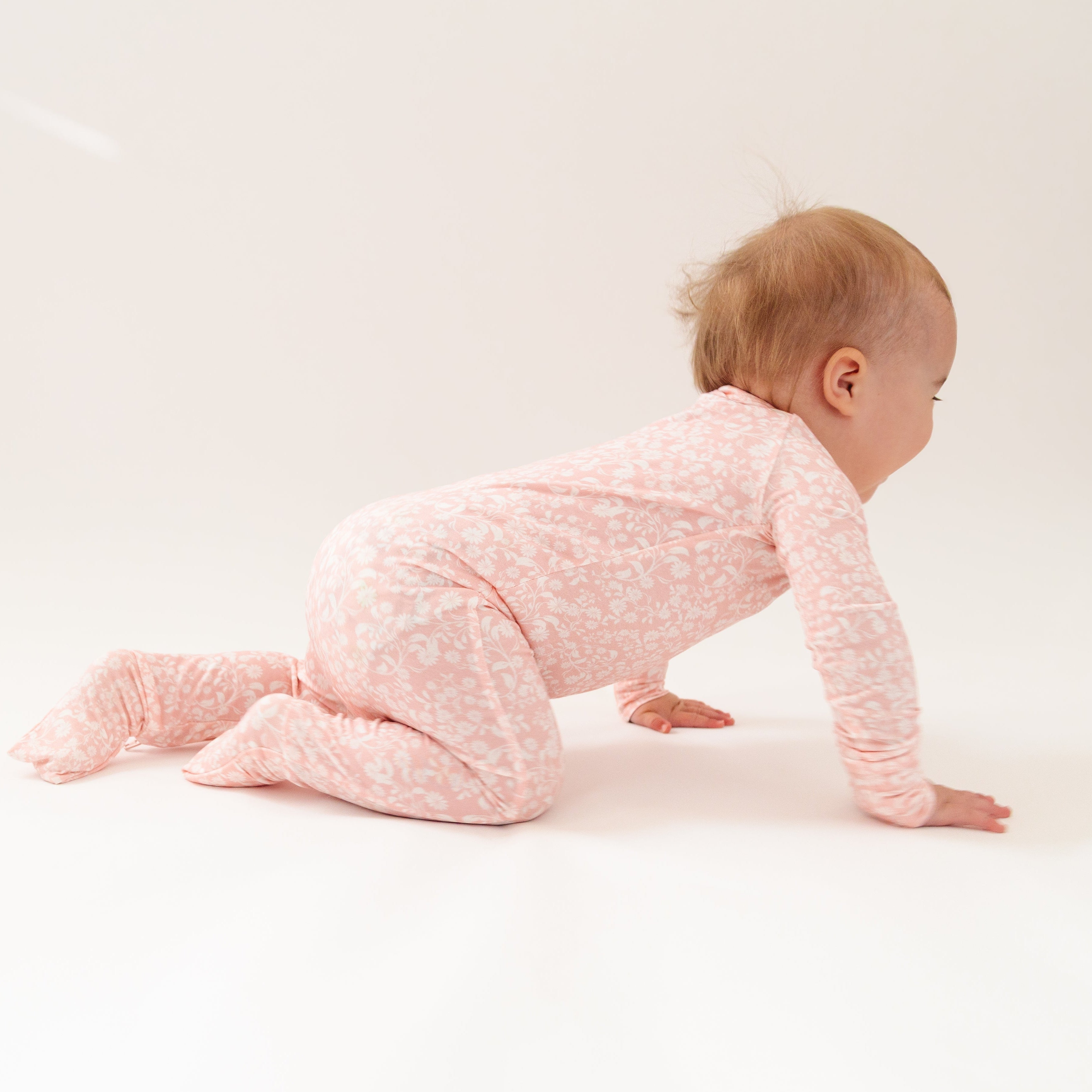 Side view of the girl crawling in the pink floral sleeper, highlighting the soft stretch and comfort