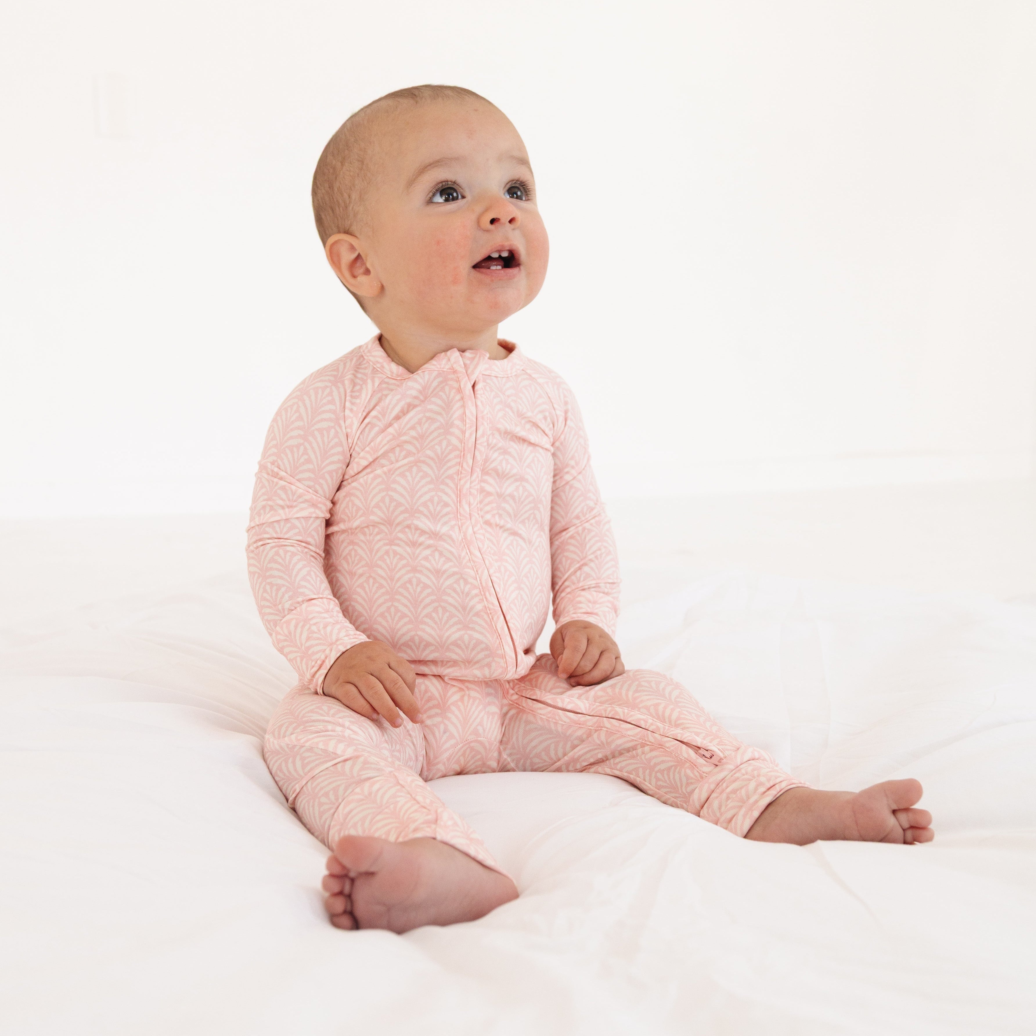 Baby girl sitting up again in the large pink floral sleeper, smiling in the vibrant pink and white print