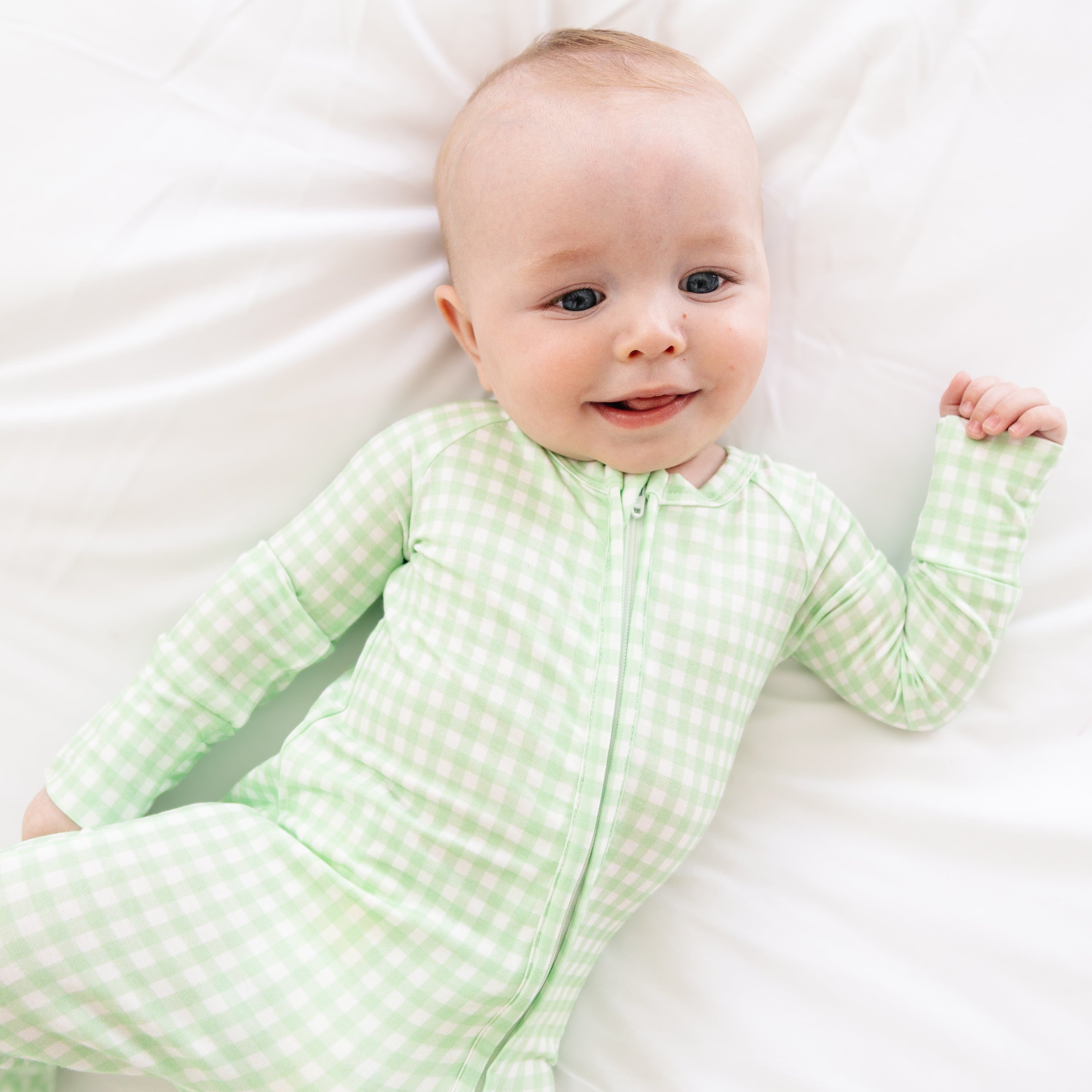 Baby baby laying down in Motette’s green checkered bamboo sleeper, smiling in the cozy, classic print