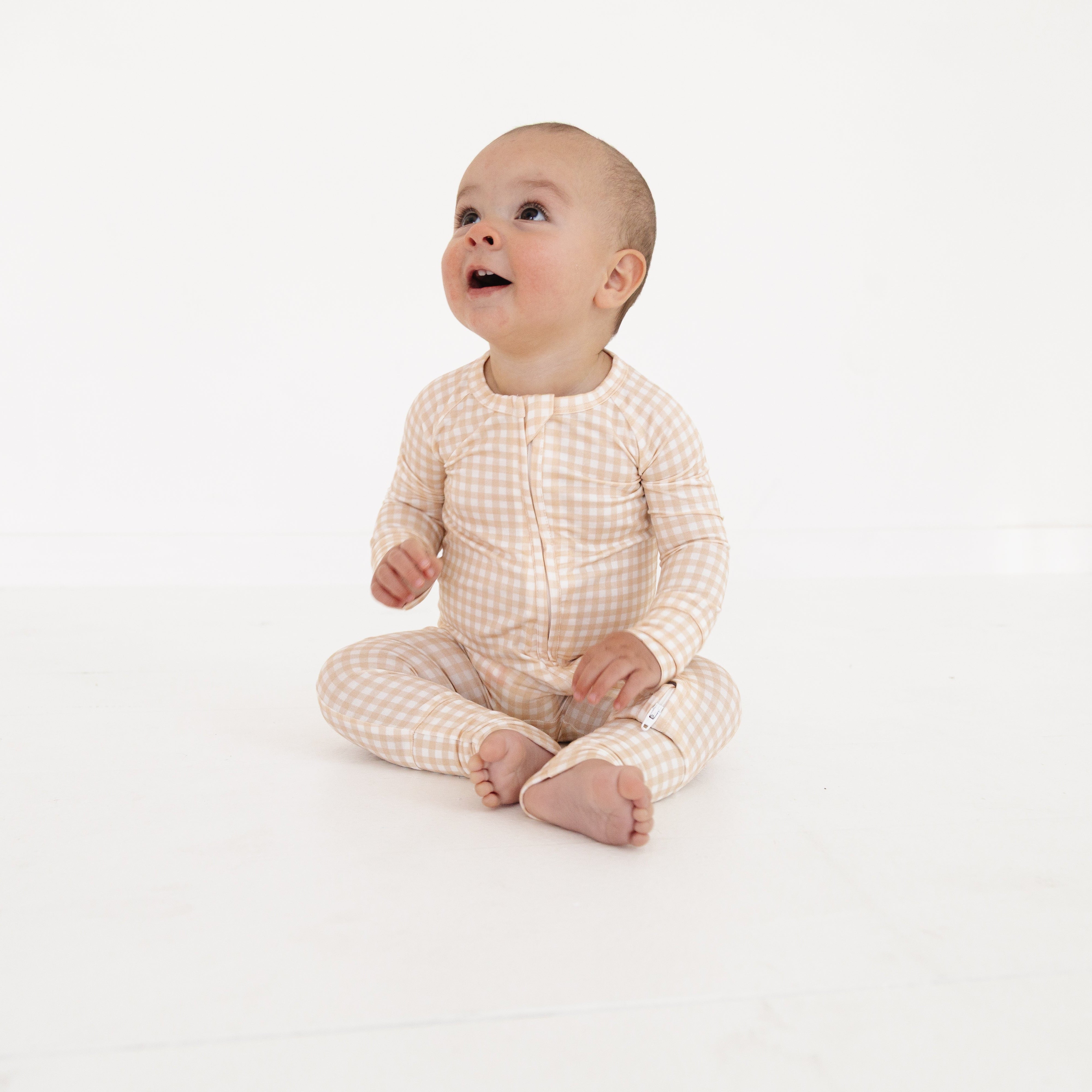 Newborn baby lounging in beige bamboo zip romper with checkered pattern, designed for comfort and movement.