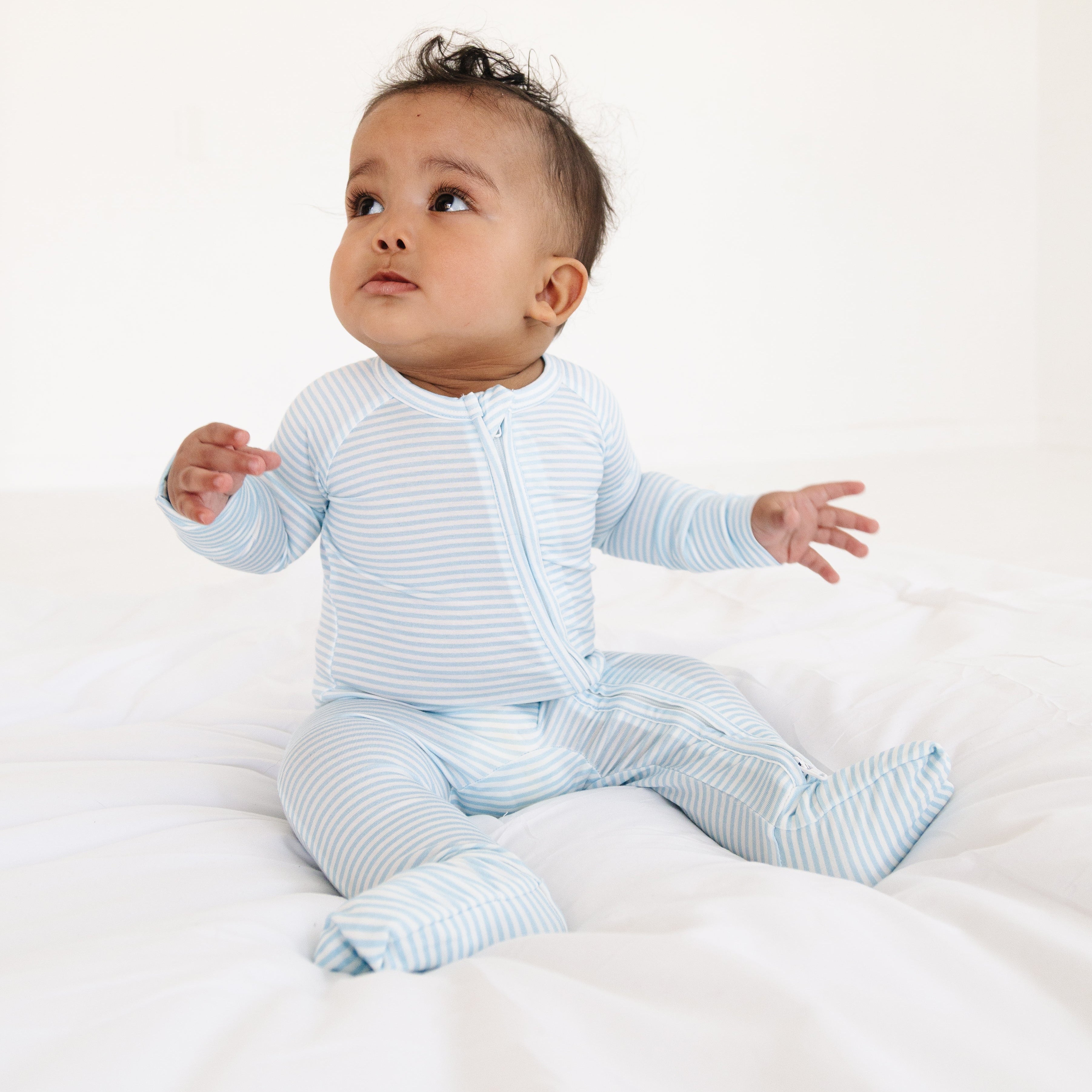 Baby boy sitting up with arms outstretched, wearing the Seaside Stripe bamboo sleeper in blue and white.