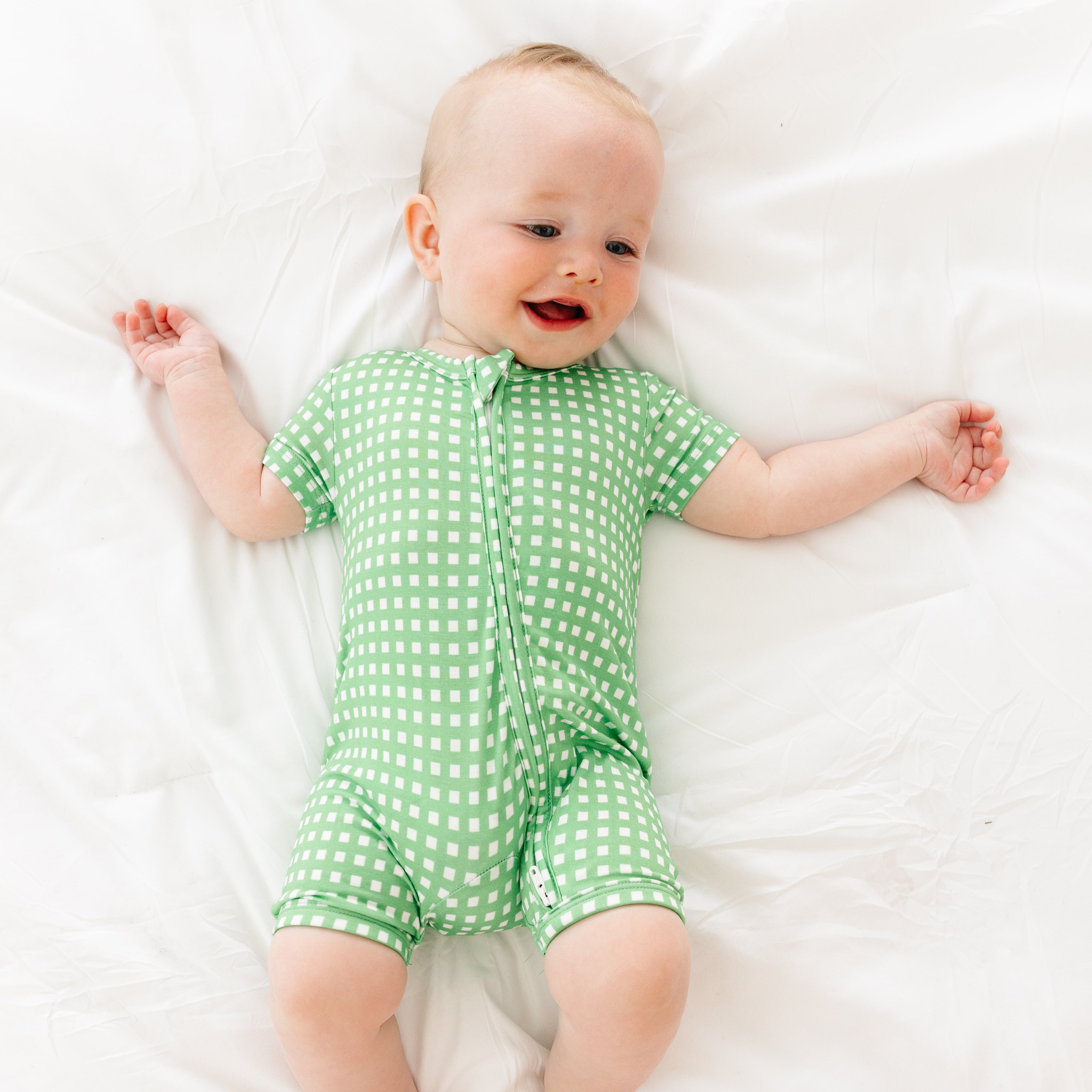 Baby smiling and playing while wearing the Garden Gingham bamboo sleeper from Motette