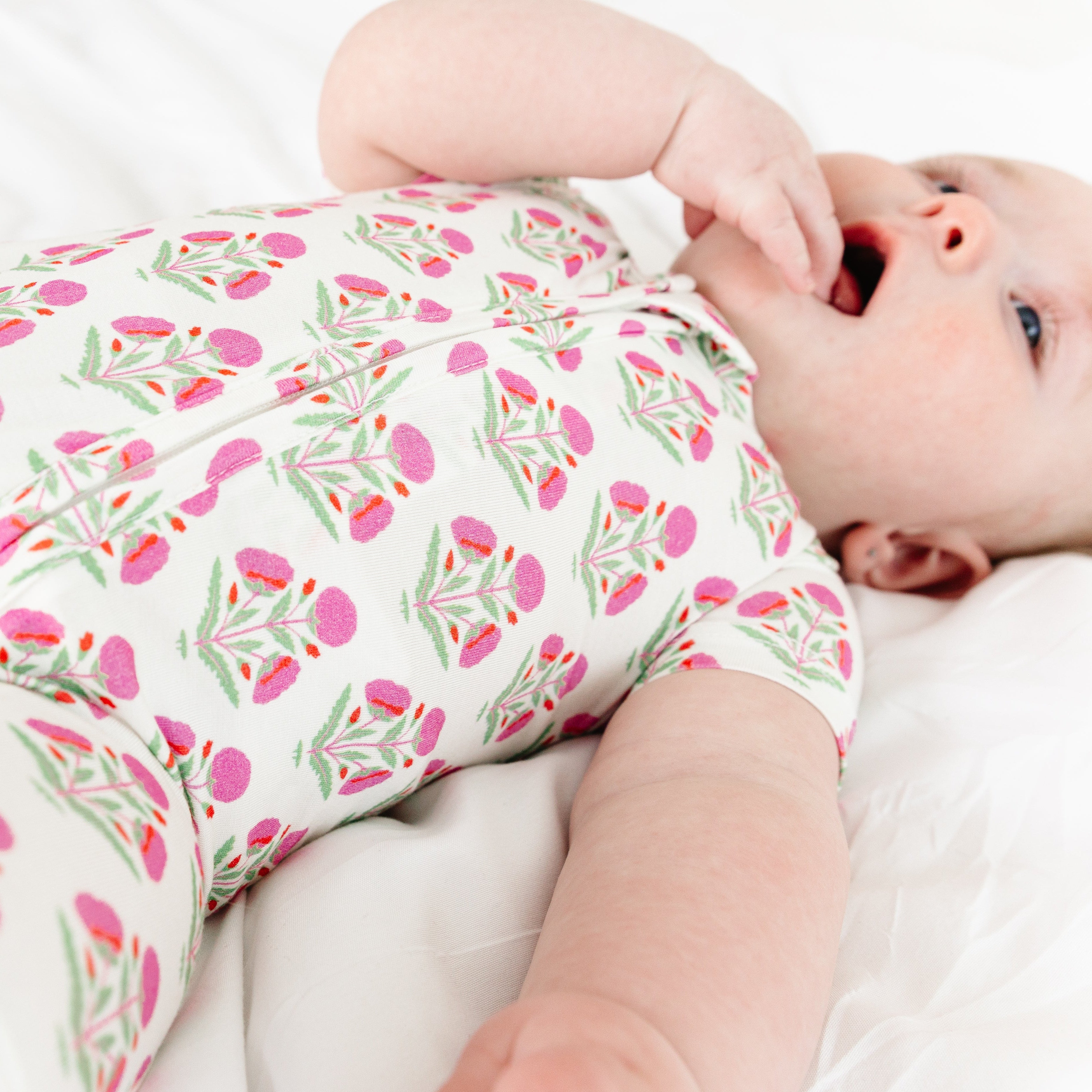 Baby smiling and playing with her hand while wearing the Pink Posy bamboo sleeper by Motette