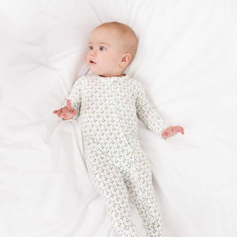 Baby resting on white sheets in Motette Lavender Lane Bamboo Sleeper, breathable bamboo pajamas.