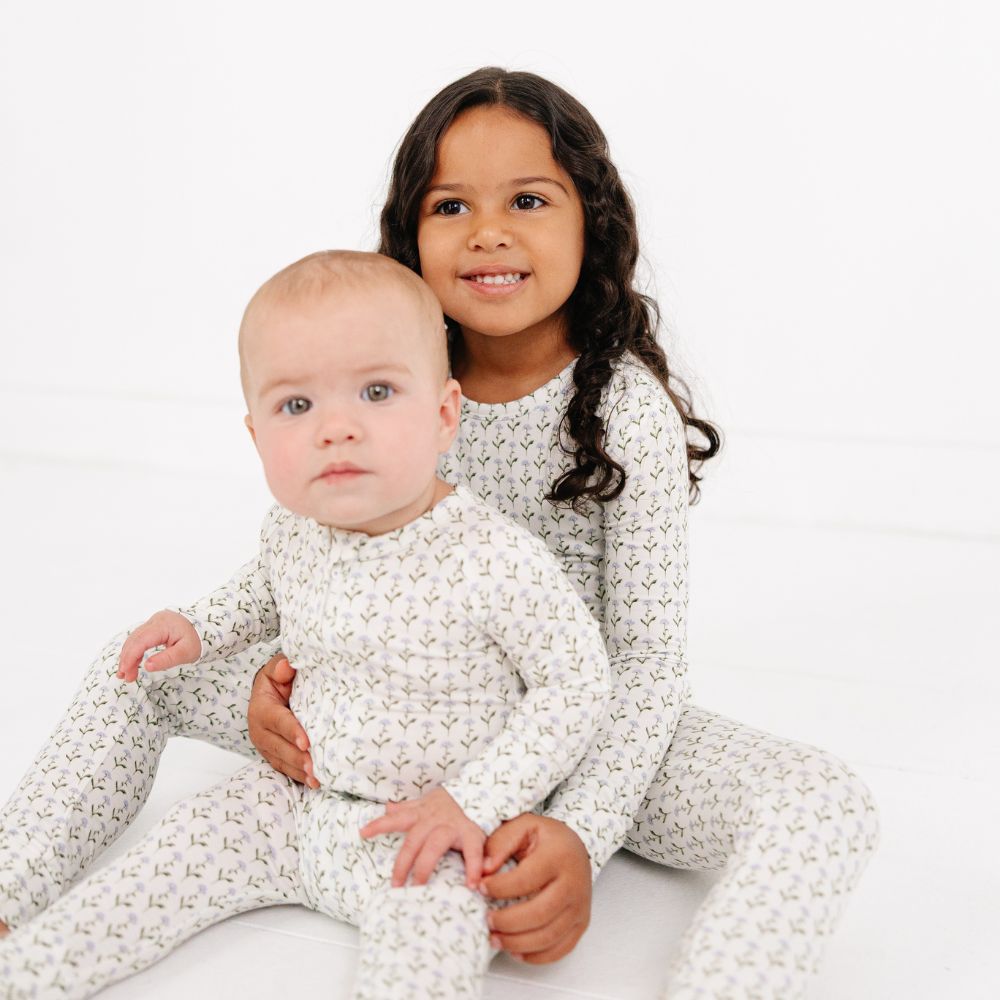 Baby and sibling sitting together wearing Motette Lavender Lane Bamboo Sleeper and matching pajamas for kids.