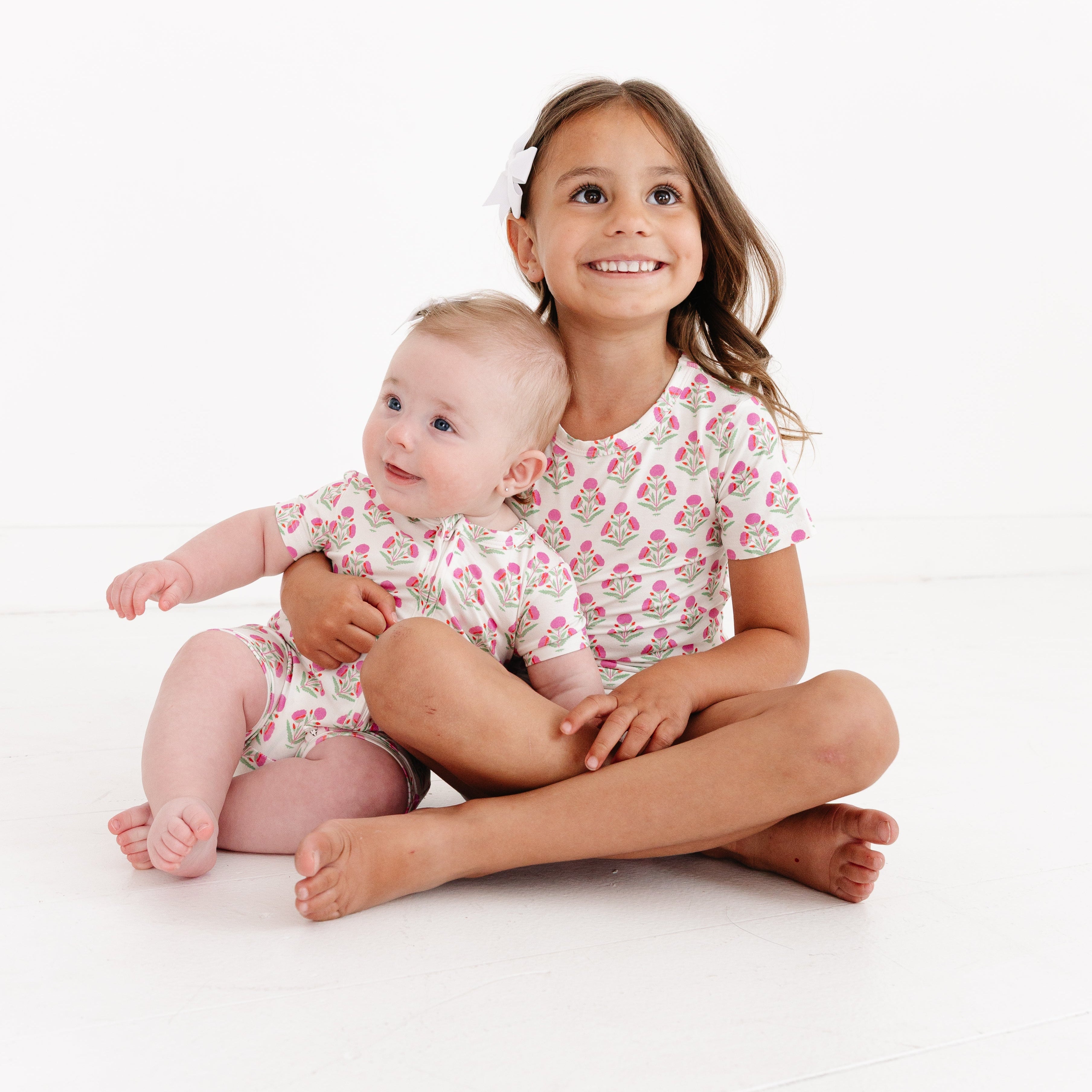 Baby wearing the Pink Posy bamboo sleeper smiling with her sister, both dressed in Motette sleepwear