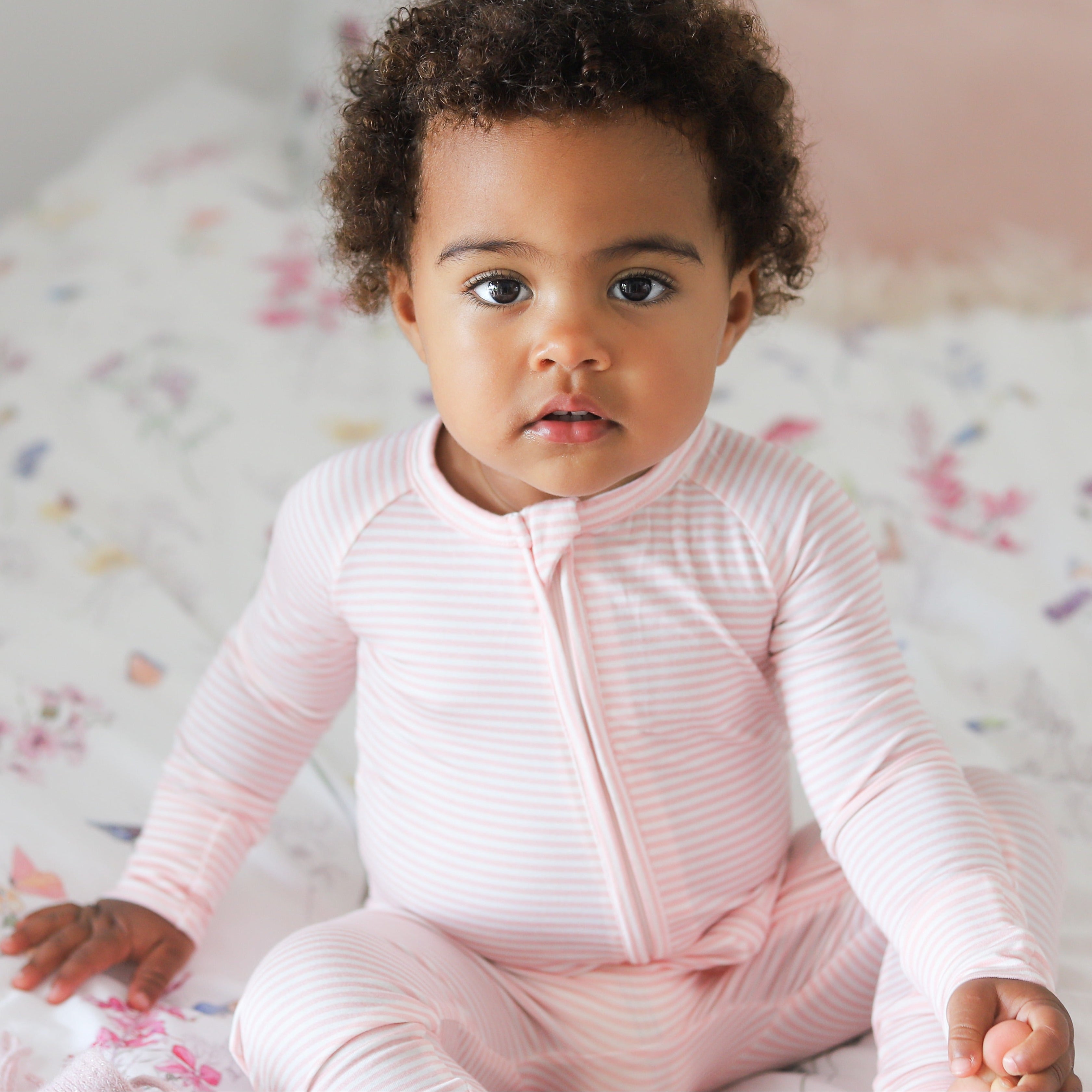 Baby girl wearing Motette peony stripe bamboo sleeper with two-way zipper and fold-over foot cuffs