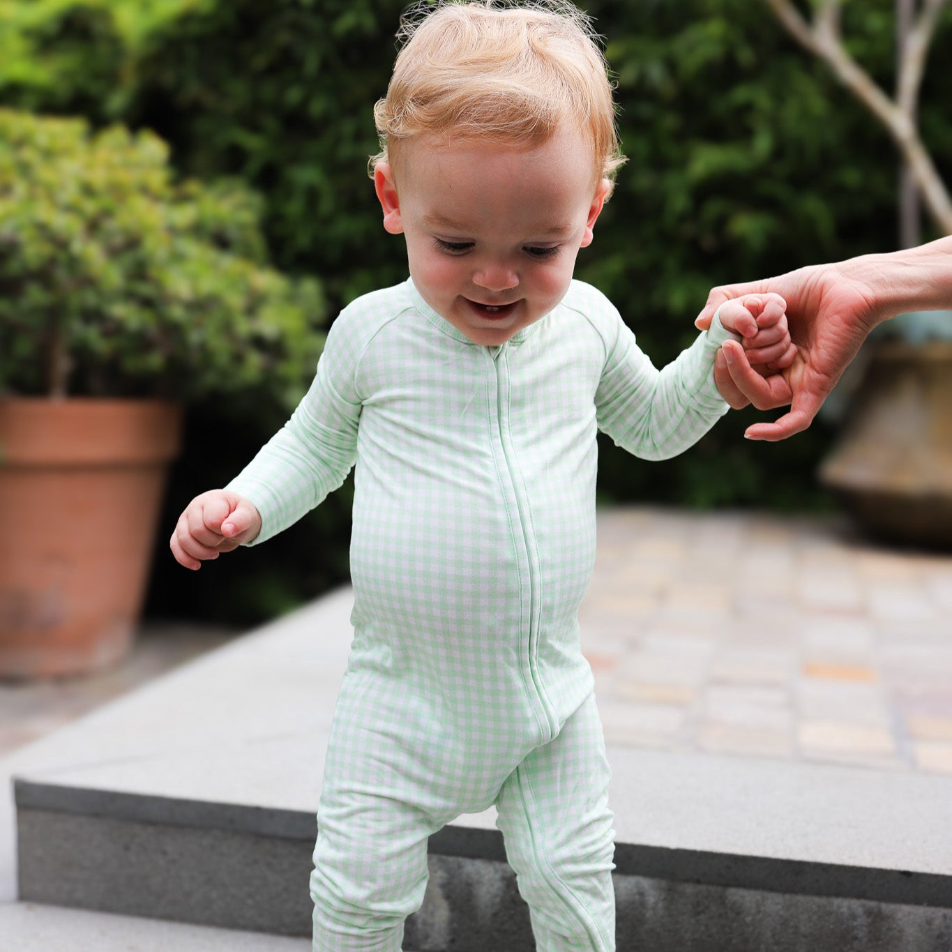 Baby boy wearing Motette green gingham bamboo sleeper with two-way zipper and fold-over feet