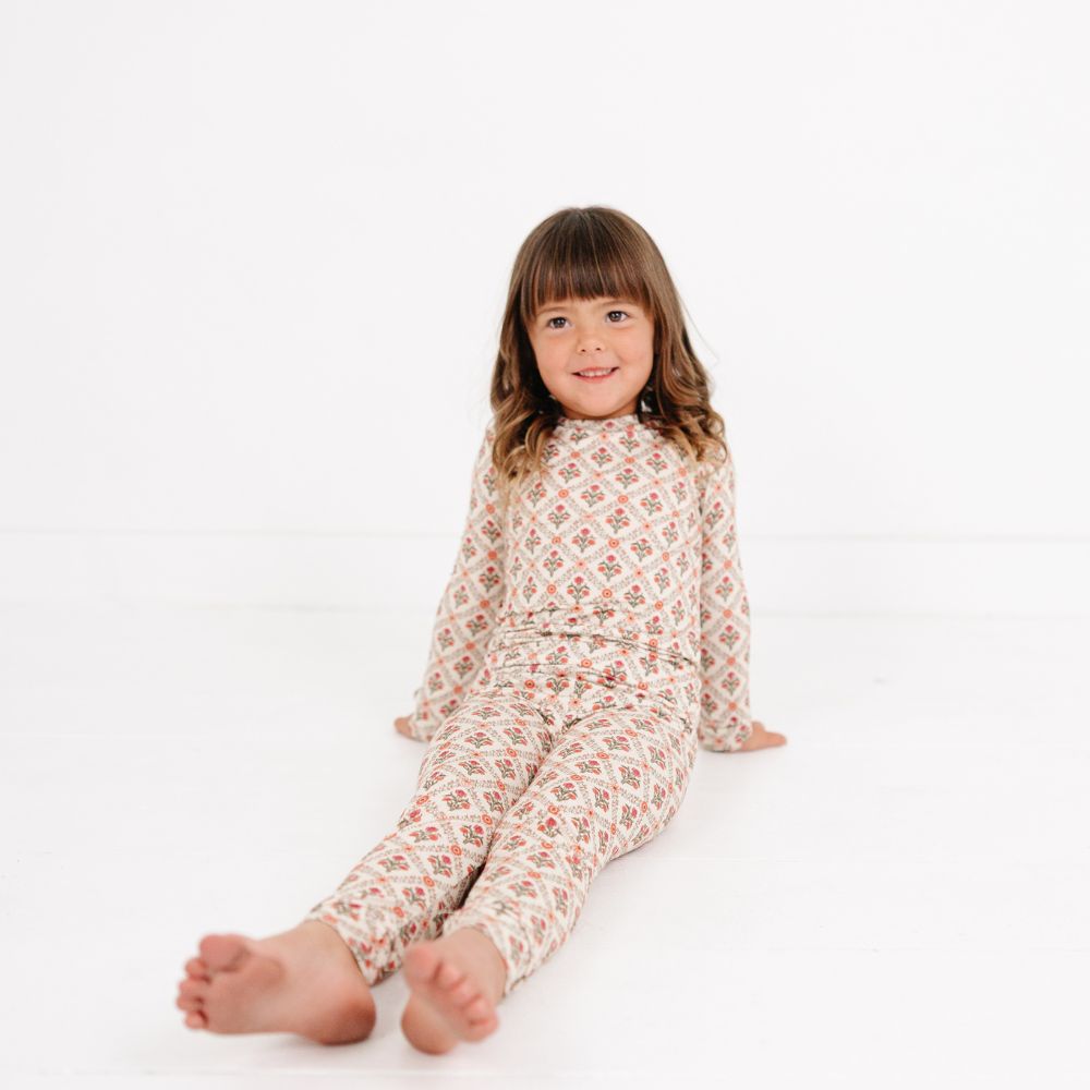 Young girl sitting with legs stretched out wearing Motette Holly Trellis Bamboo Kids Pajama Set.