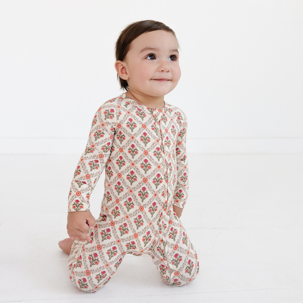 Baby smiling while kneeling wearing the Motette Holly Trellis Bamboo Sleeper, featuring a delicate coral flower and green leaf trellis pattern on a high-quality cream bamboo material.