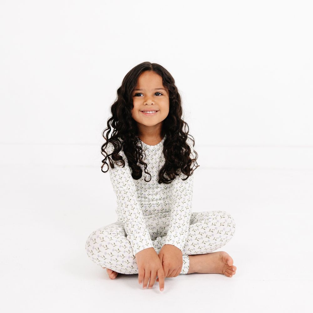 Little girl sitting cross-legged and smiling wearing Motette Lavender Lane Bamboo Kids Pajama Set.