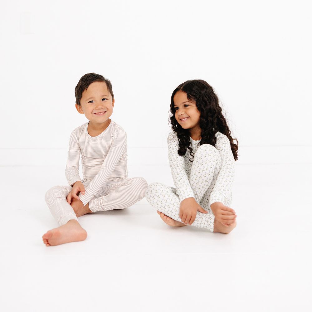 Boy and girl sitting on floor smiling, both wearing Motette Bamboo Pajamas in Oatmeal Stripe and Floral prints.