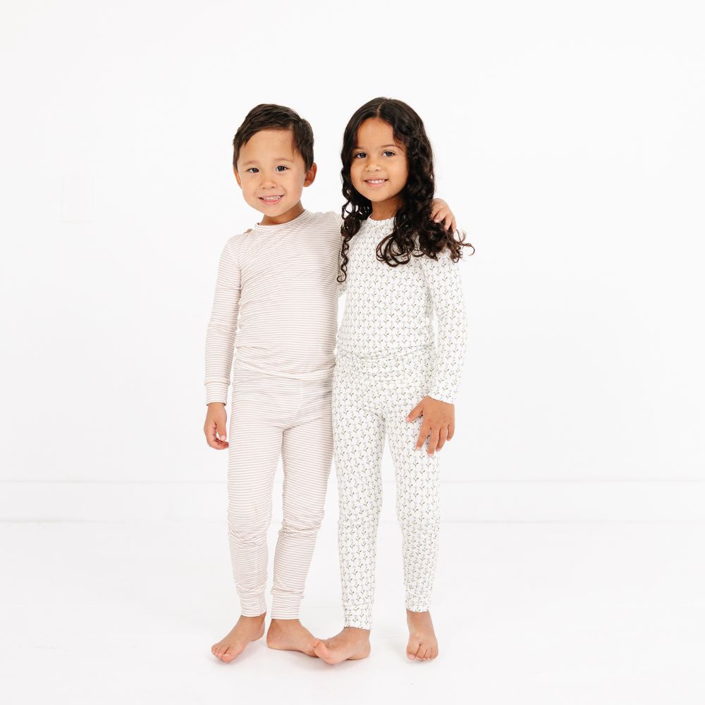 Boy in Motette Oatmeal Stripe Bamboo Pajama Set standing beside girl in floral print pajamas, smiling together.