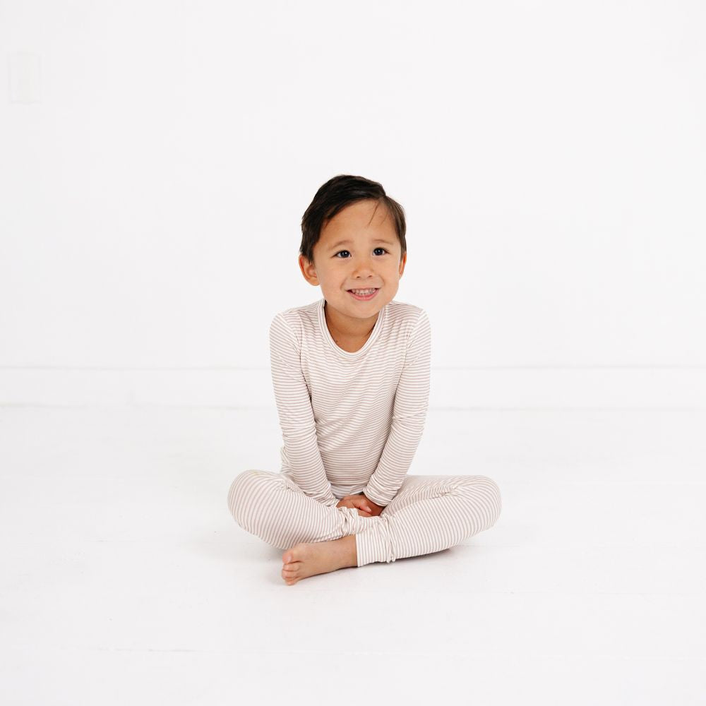 Boy sitting cross-legged on floor wearing Motette Oatmeal Stripe Bamboo Kids Pajama Set.