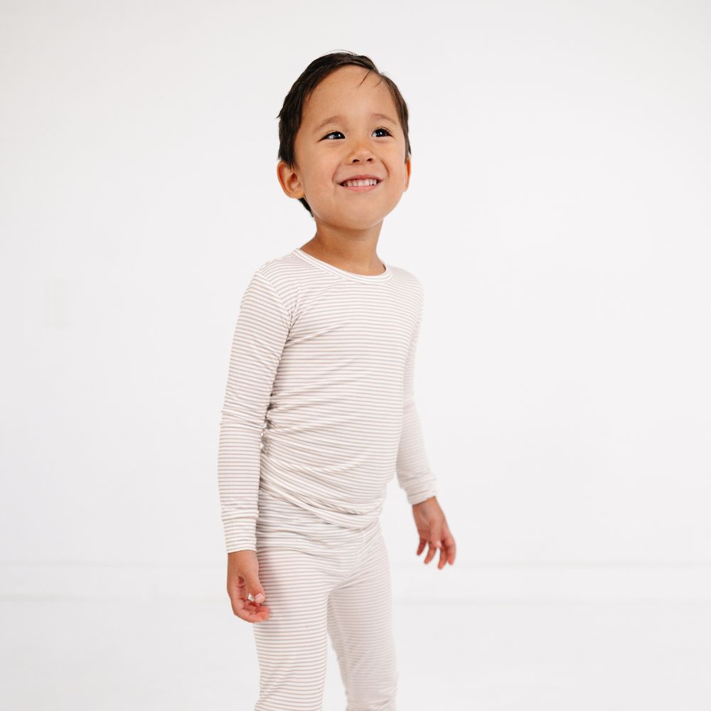 Boy smiling and looking sideways while standing in Motette Oatmeal Stripe Bamboo Kids Pajama Set.