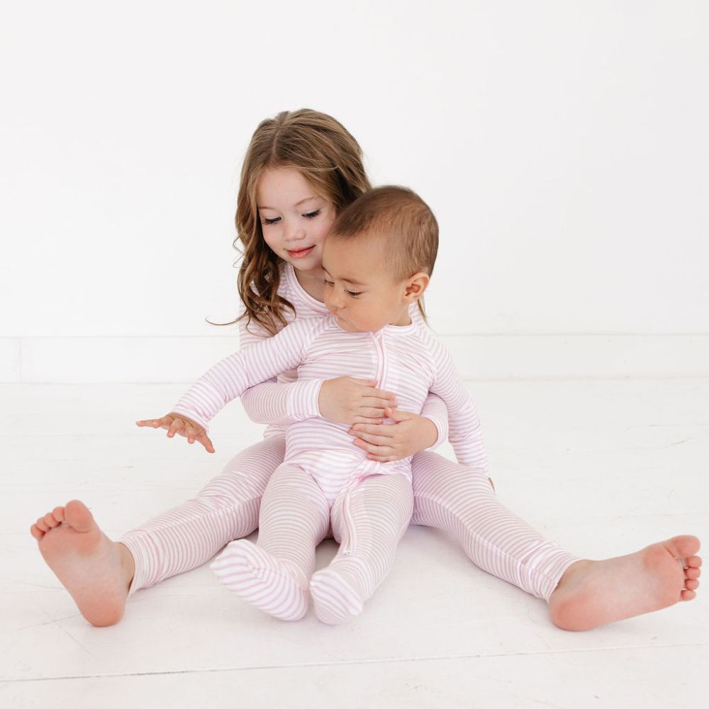 Older sister holding baby sibling in matching Ballet Stripe bamboo pajamas – perfect coordinated sibling set by Motette