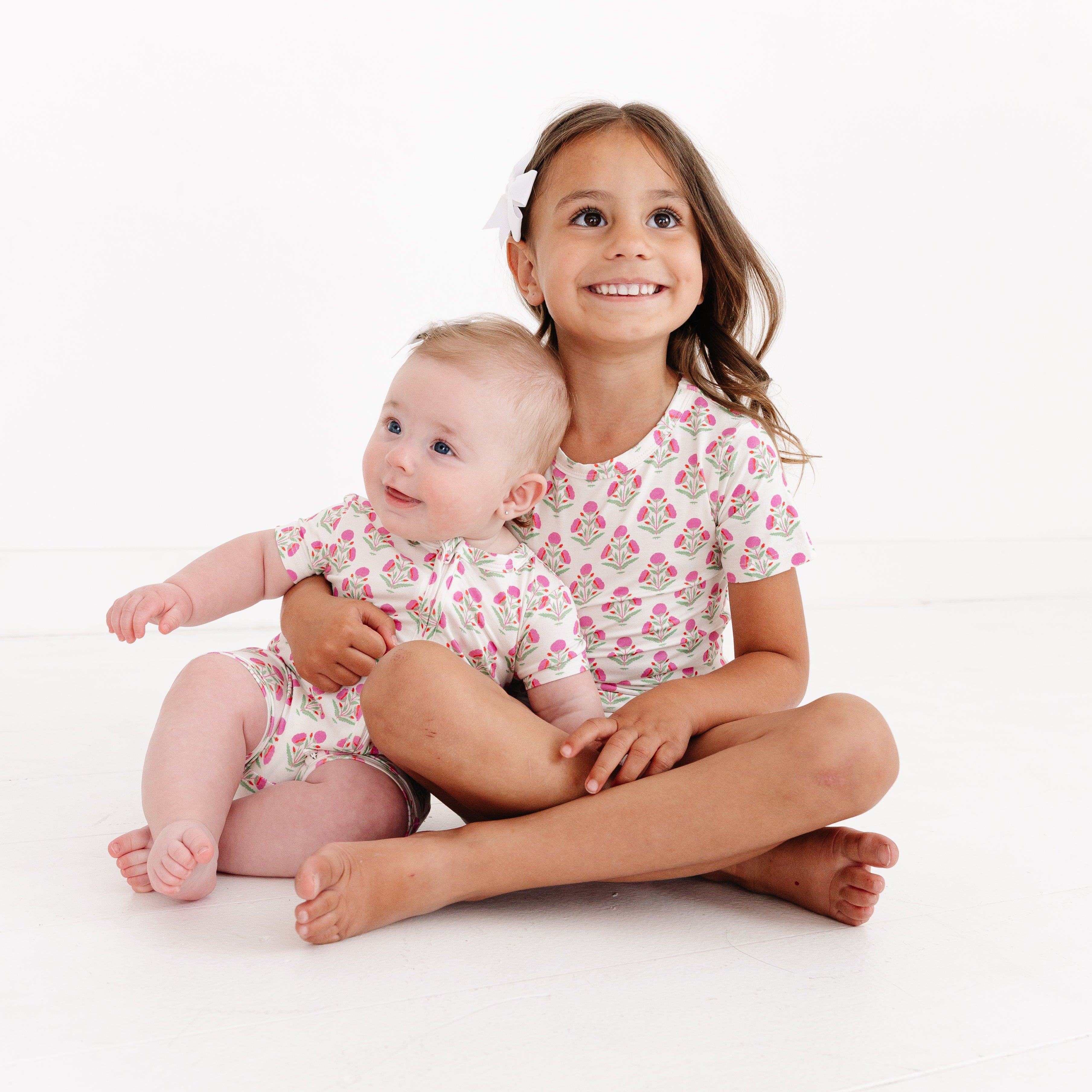 Toddler girl and her baby sister wearing matching Pink Posy bamboo pajama sets from Motette