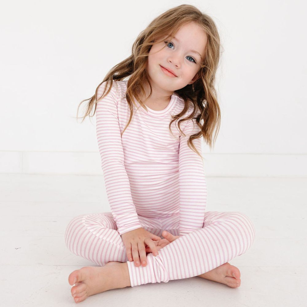 Toddler girl sitting cross-legged in Ballet Stripe bamboo pajamas – comfy and eczema safe toddler pajamas by Motette