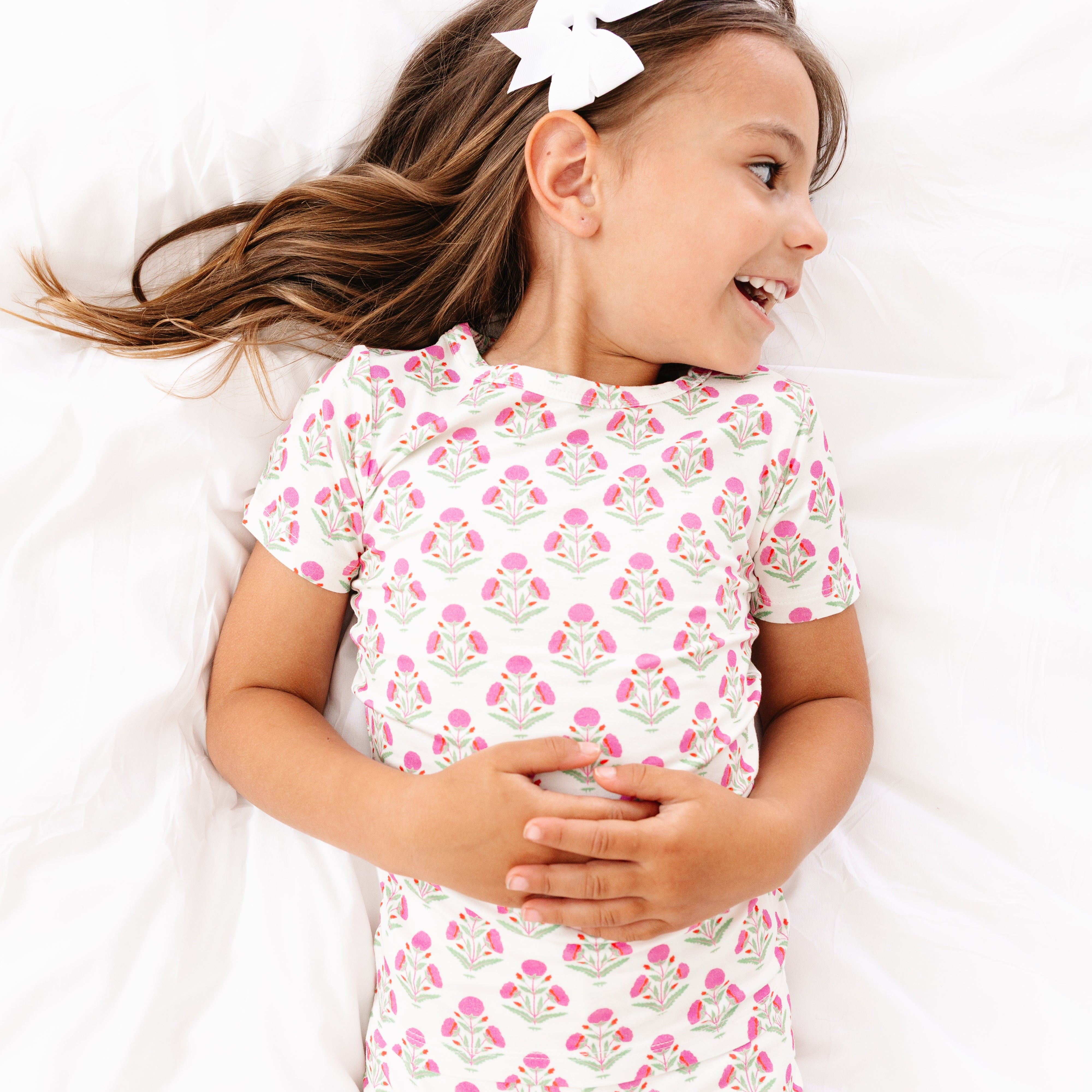 Toddler girl smiling while lying down in the Pink Posy bamboo pajama set by Motette