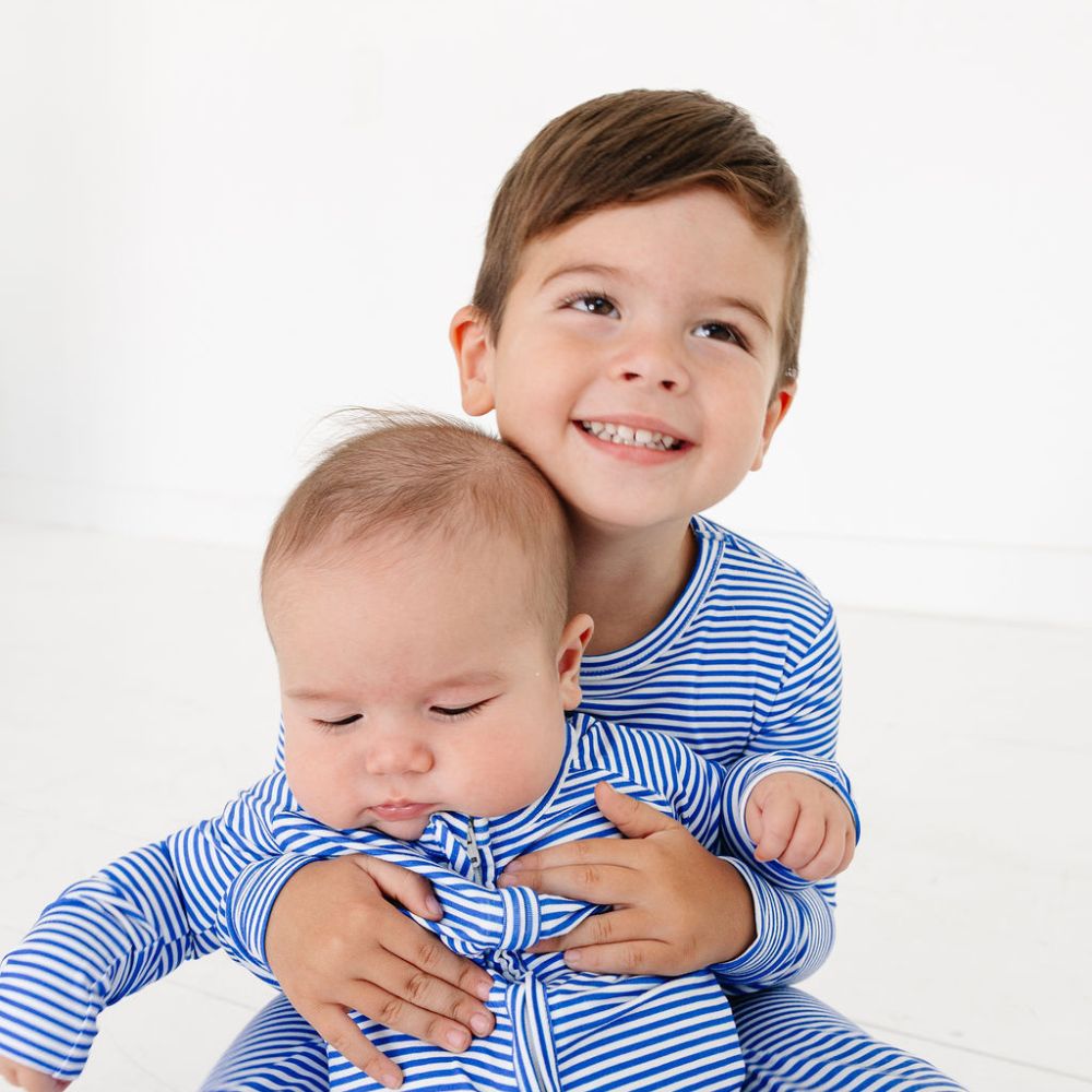 Toddler hugging baby sibling while wearing matching bamboo pajamas in Cobalt Stripe by Motette – coordinated sibling set for sensitive skin