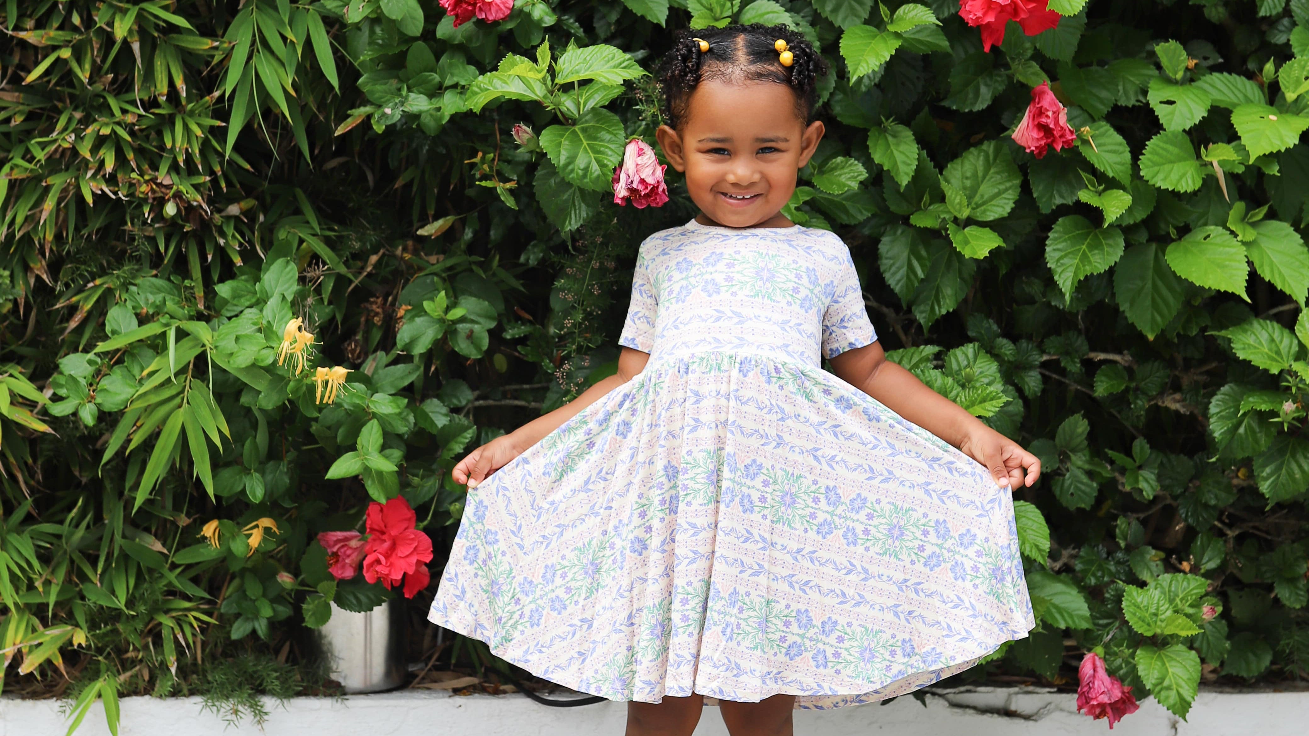 Young girl wearing Motette’s bamboo pink and purple dress, smiling and twirling outdoors, showcasing the dress’s soft, flowy fabric and playful design.