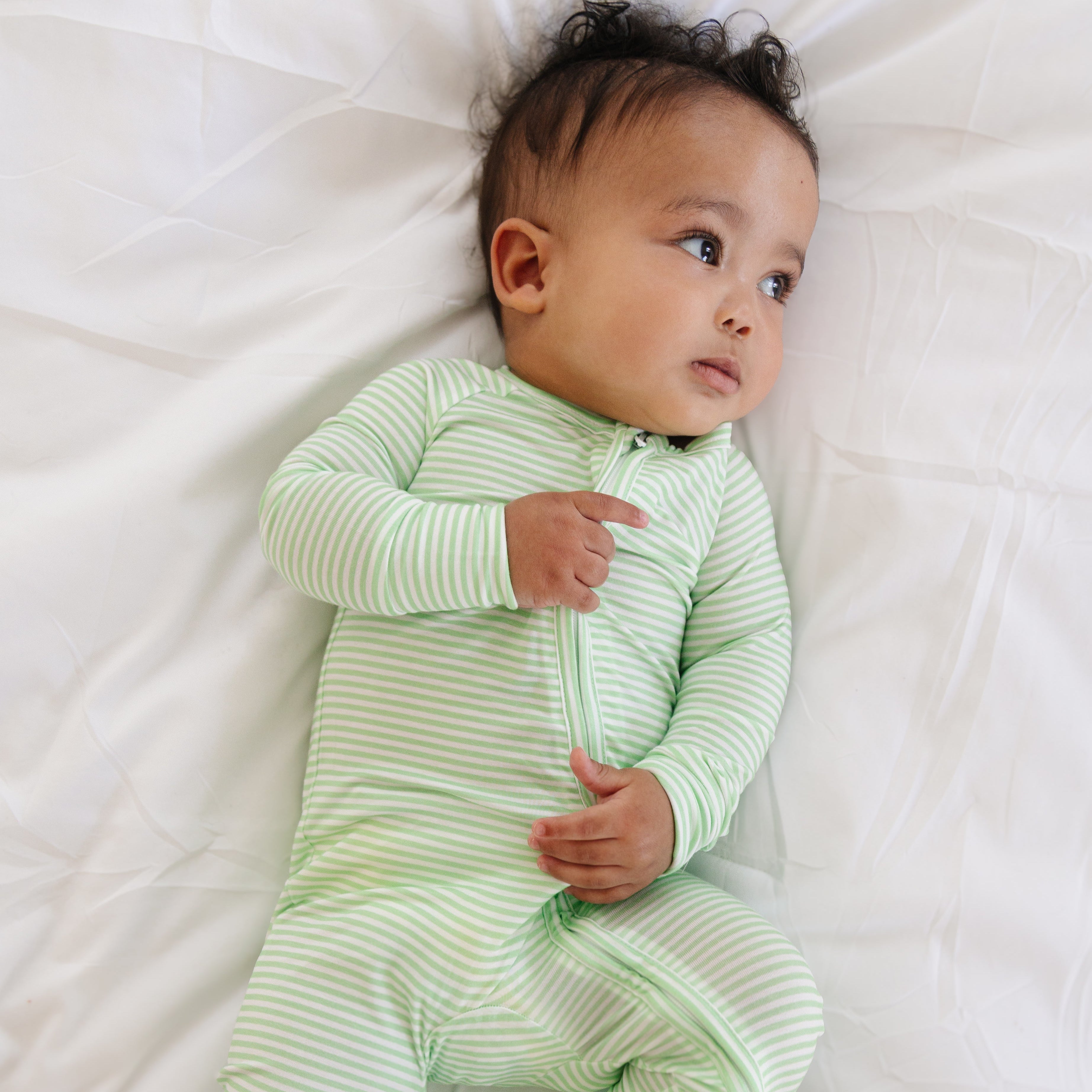 Baby laying down in Motette’s green striped bamboo sleeper, with cozy cuffs and a two-way zipper visible