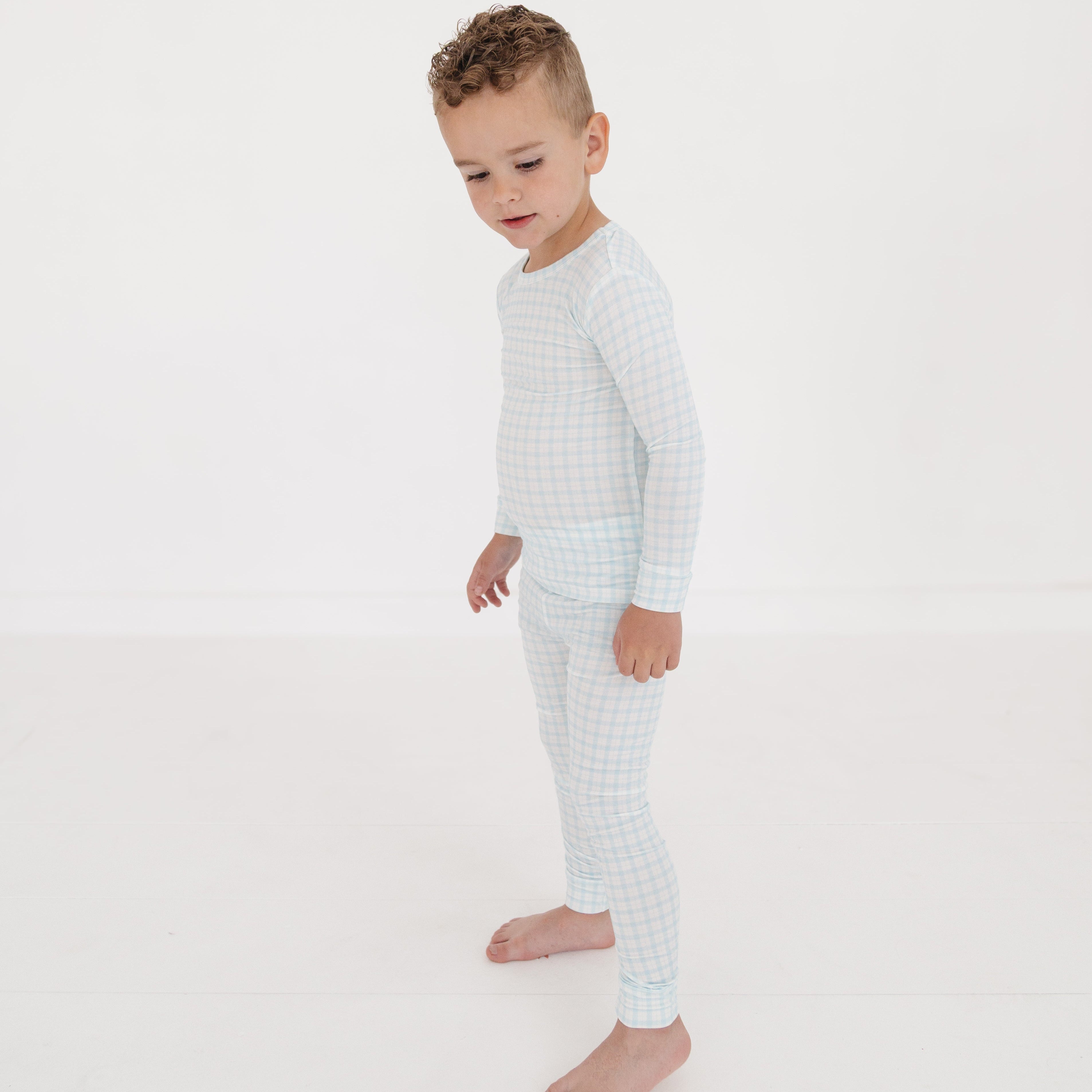 Toddler boy standing in blue and white checkered bamboo two-piece pajamas, smiling and facing to the side