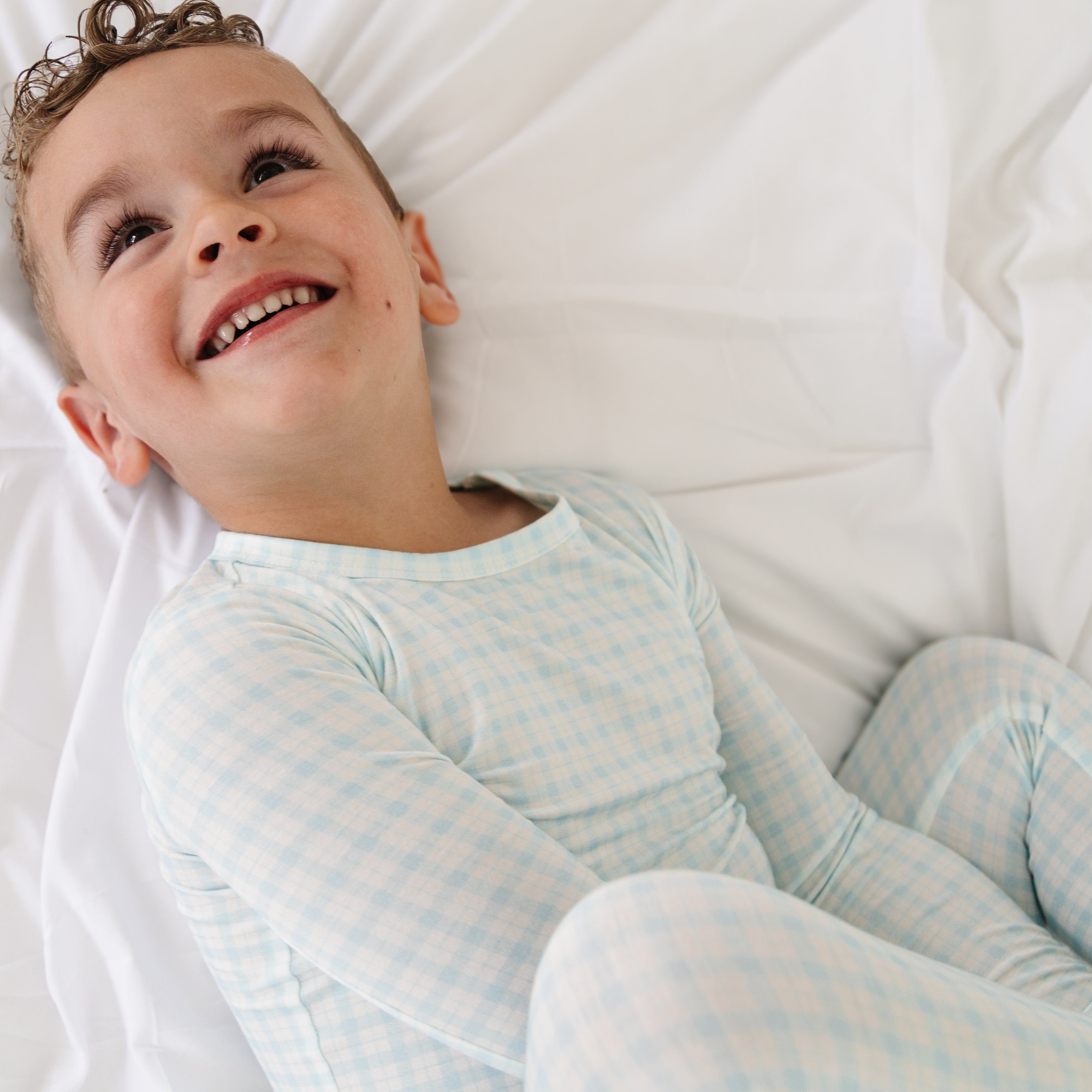 Toddler boy lying down in blue checkered bamboo pajamas, looking up with a relaxed expression.
