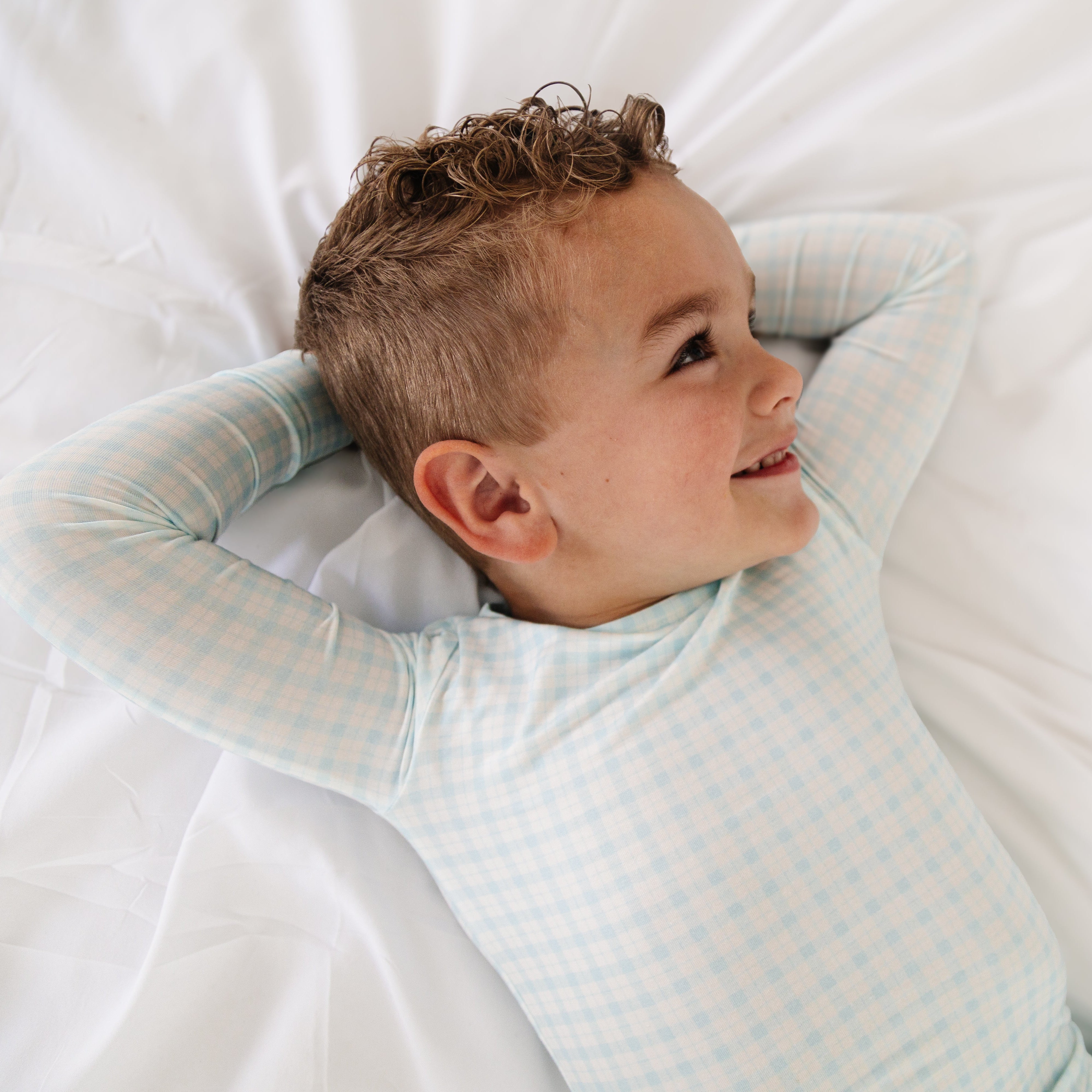 Side view of toddler boy laying in blue and white check pajama set, showing fit and comfort.