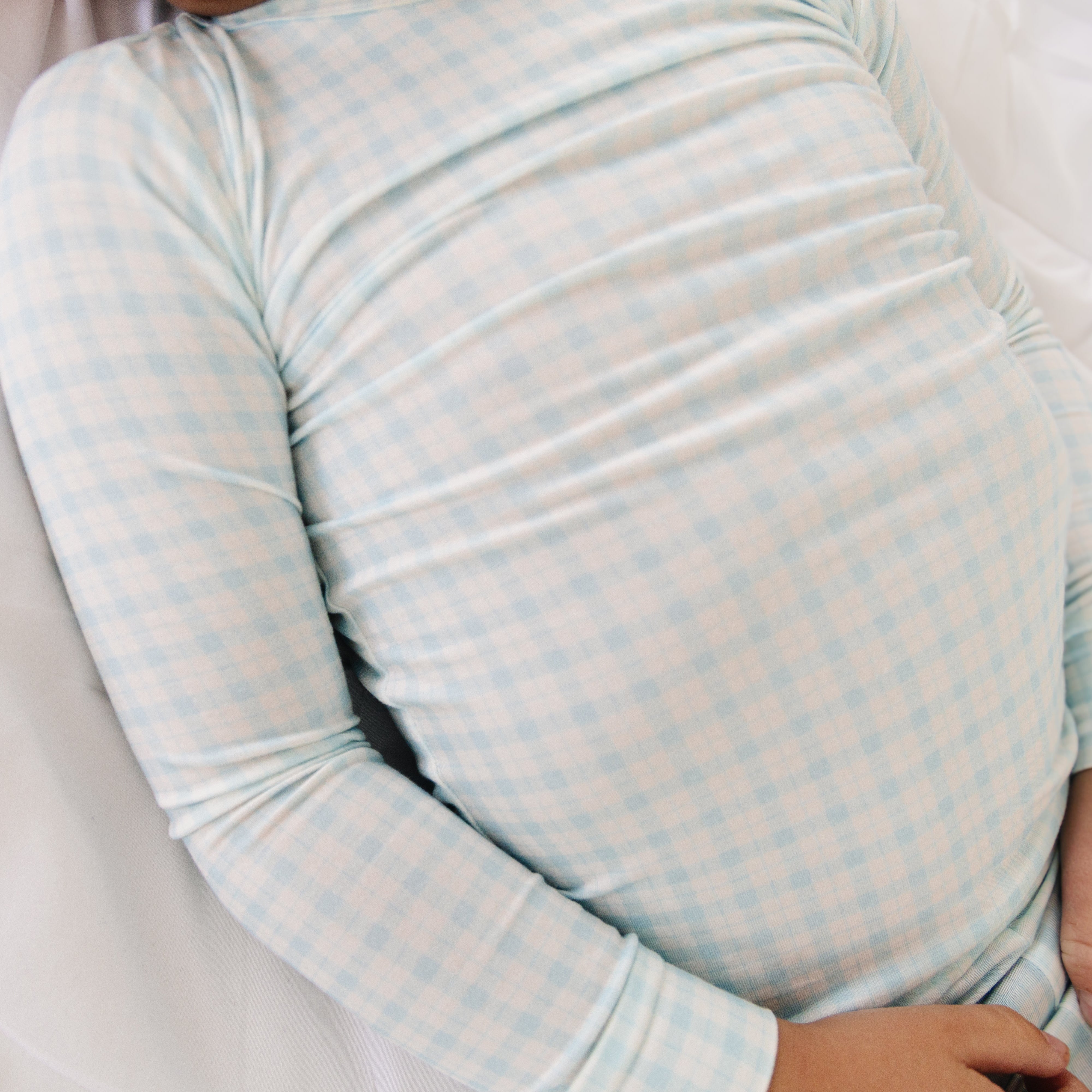 Overhead shot of toddler boy resting in blue checkered two-piece bamboo pajamas, highlighting soft stretch fabric.