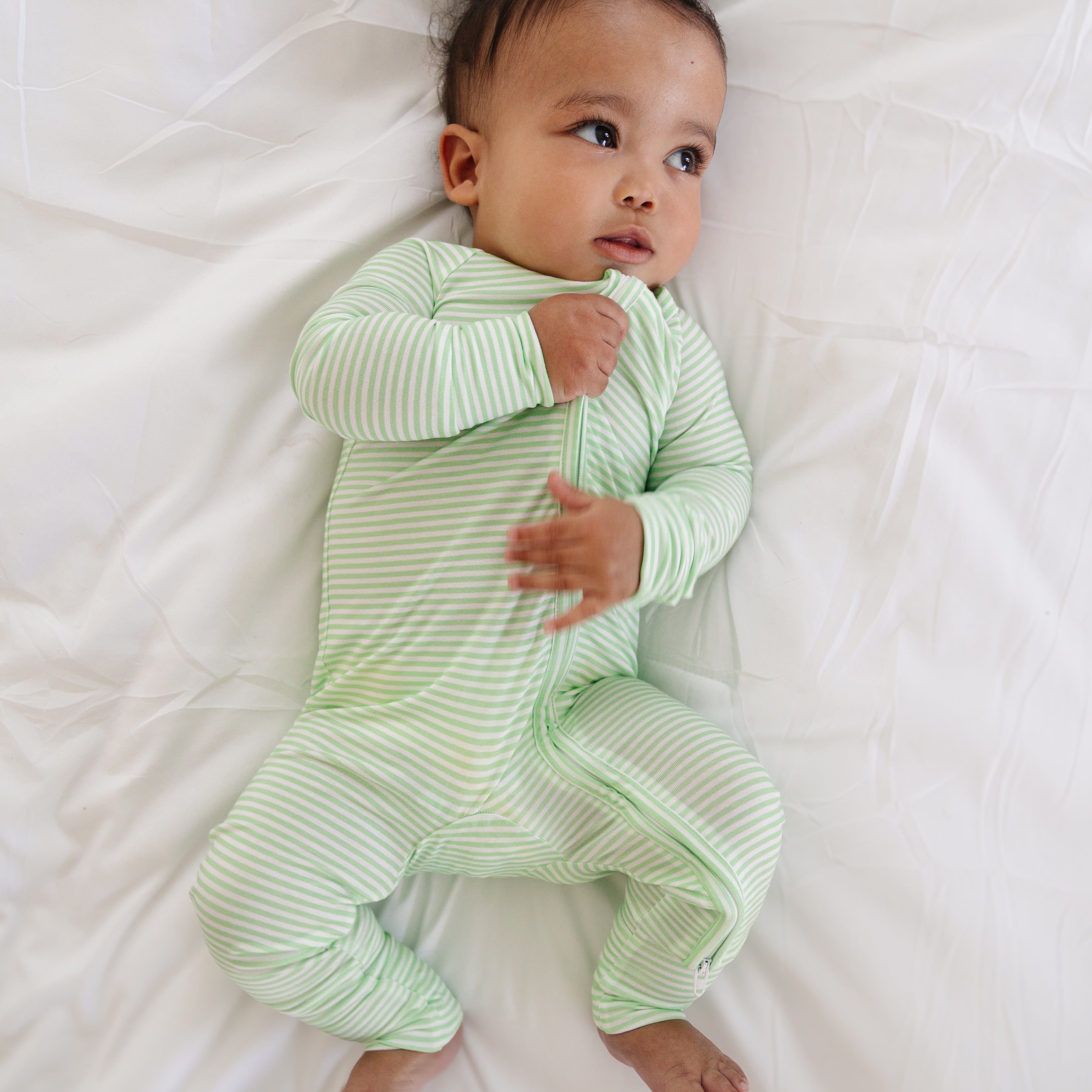 Baby boy laying down in the Pear Stripe bamboo sleeper, showing the full-body fit and soft green and white stripes.
