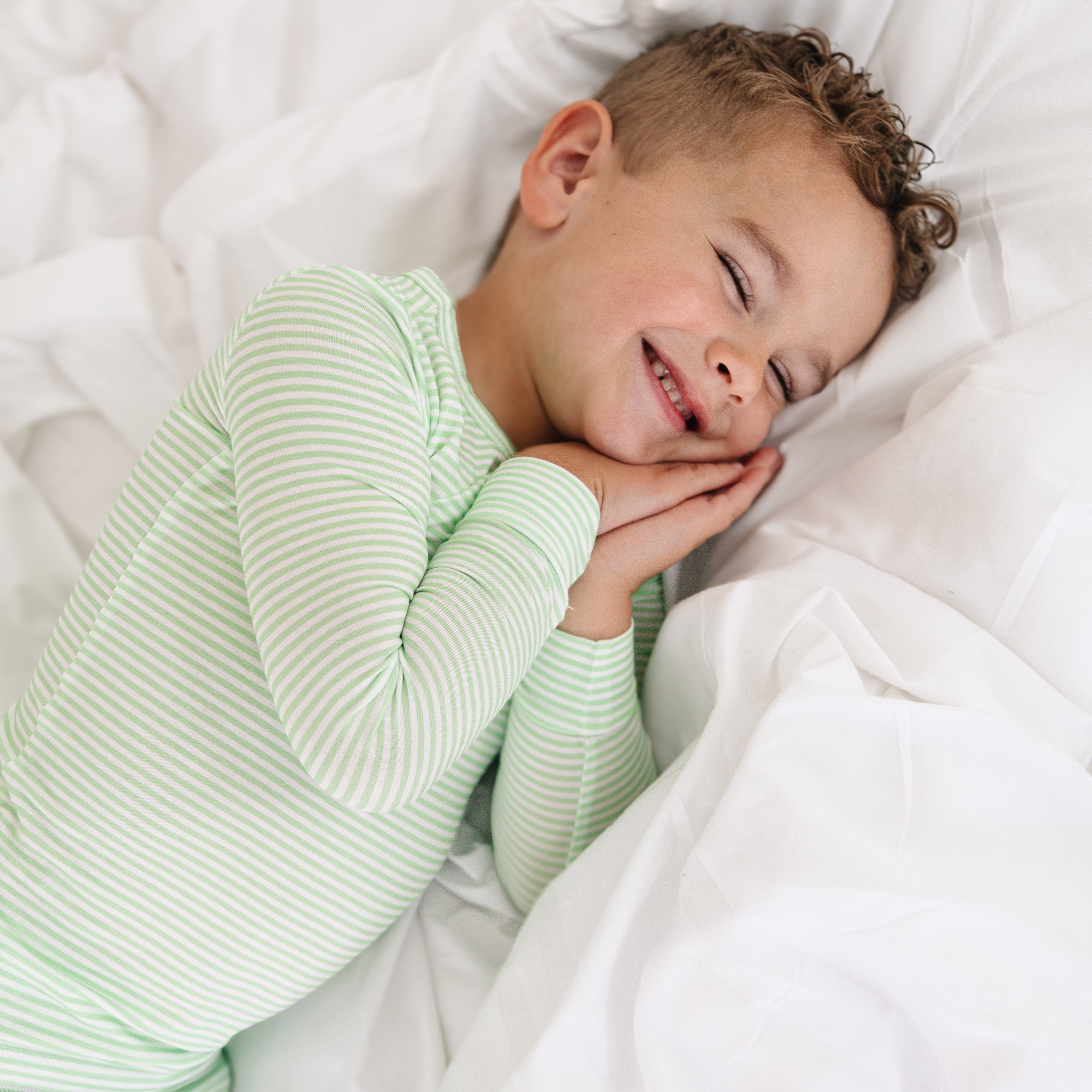 Toddler lounging in green striped bamboo pajamas, highlighting breathable fabric and comfy design.