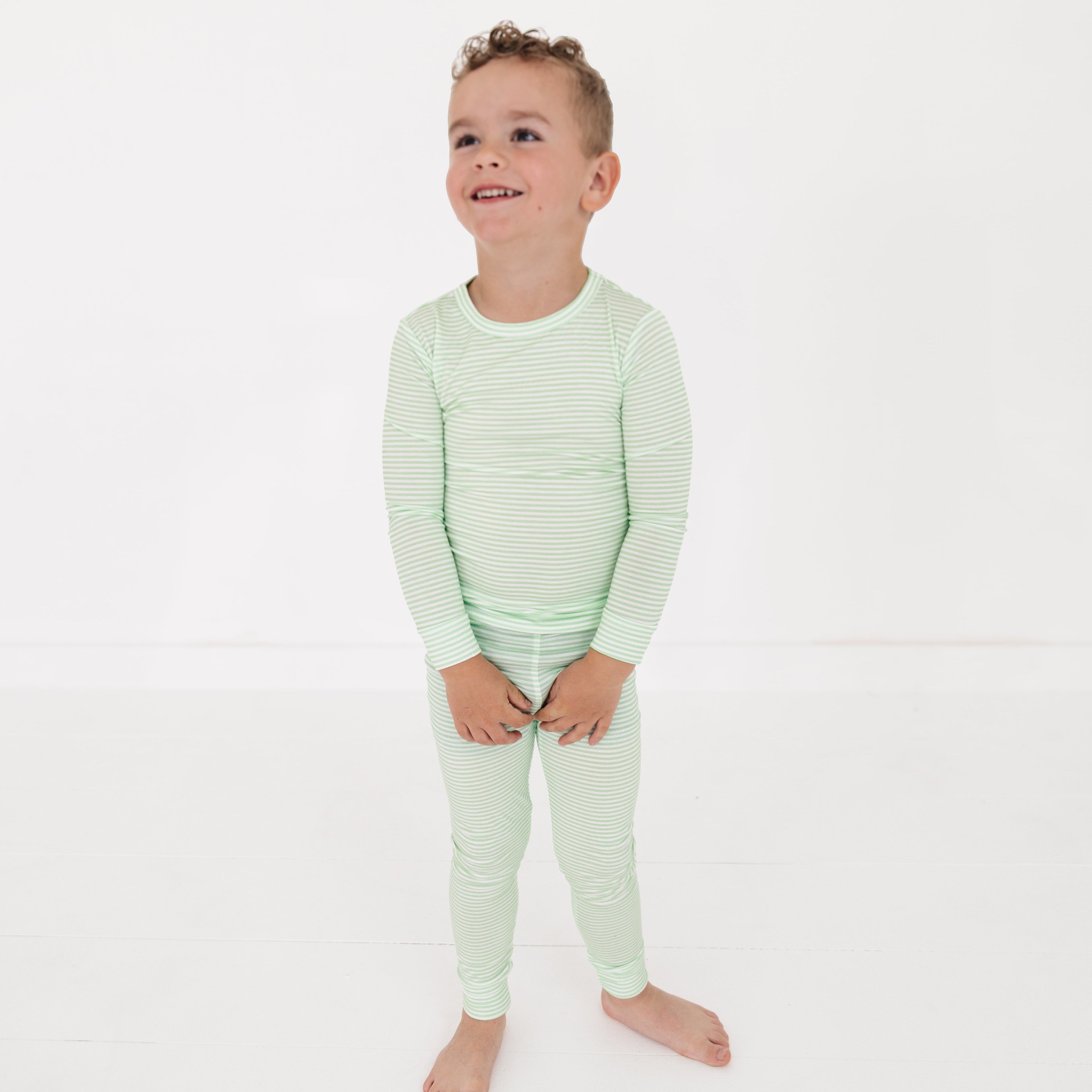 Toddler wearing green stripe bamboo pajama set, smiling and standing in a bright, cozy room.