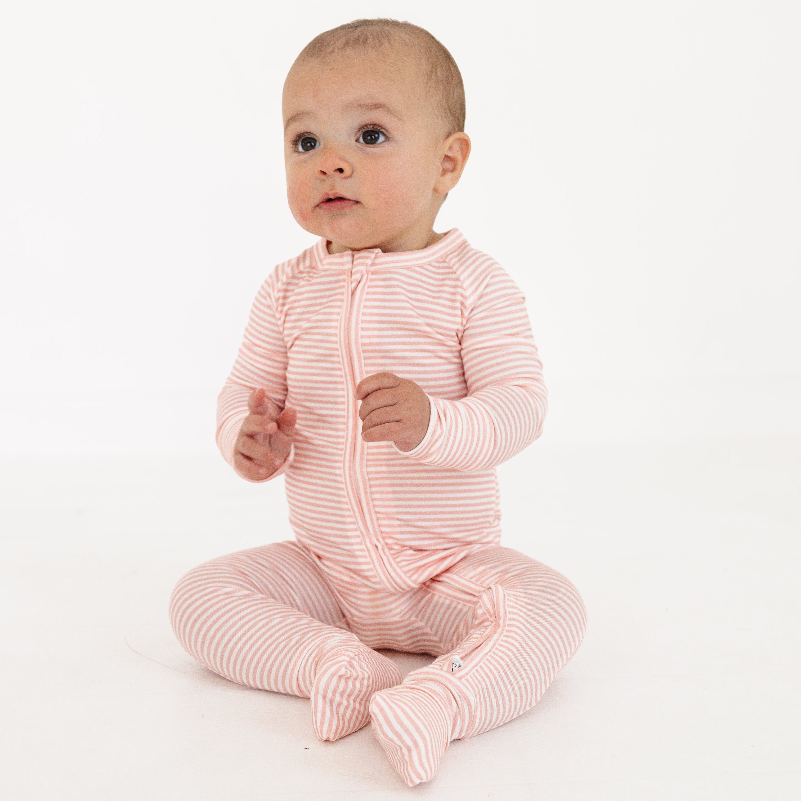 Baby girl sitting up again in the pink stripe sleeper, looking cozy and content