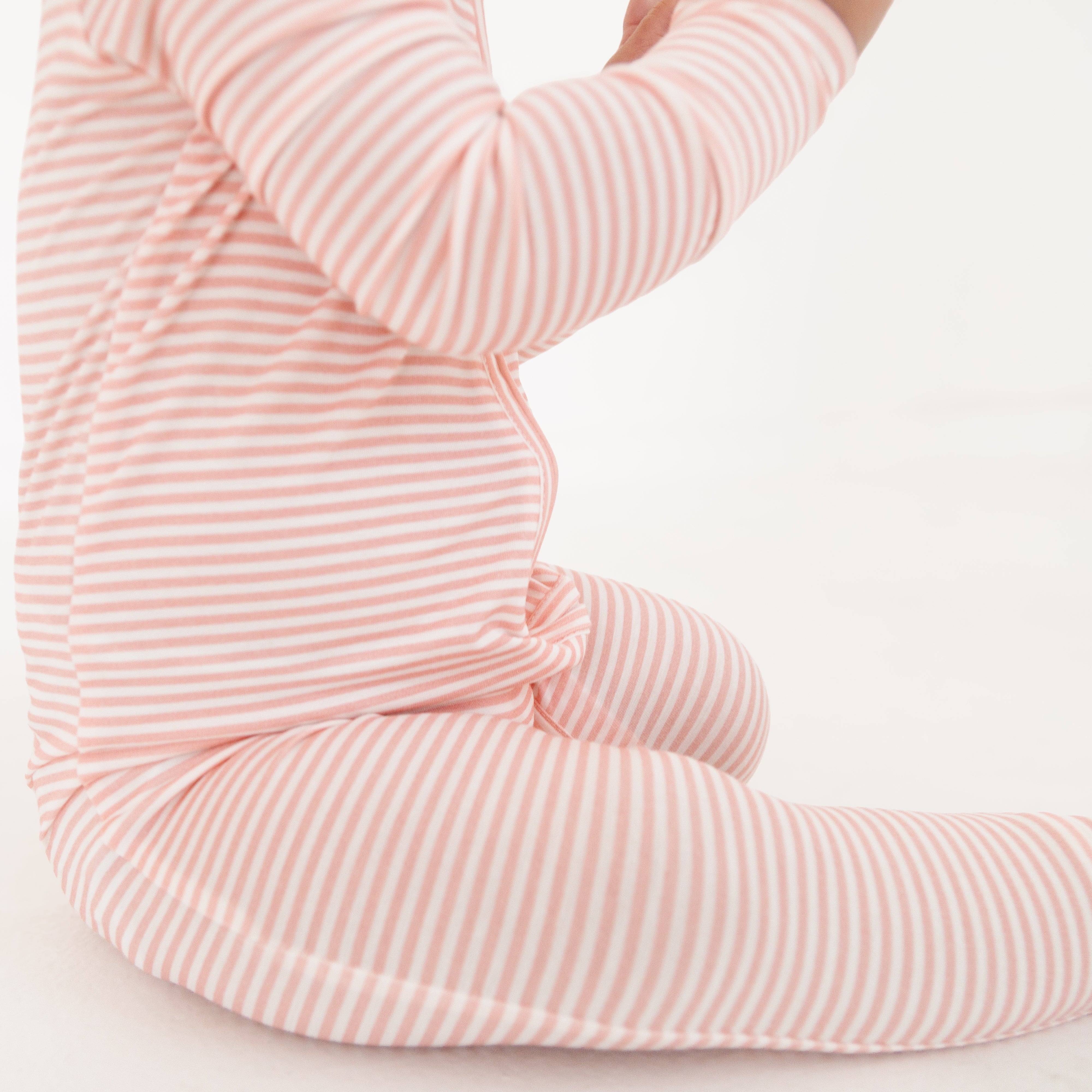 Profile view of the baby crawling in the pink stripe sleeper, highlighting the footed design and flexibility