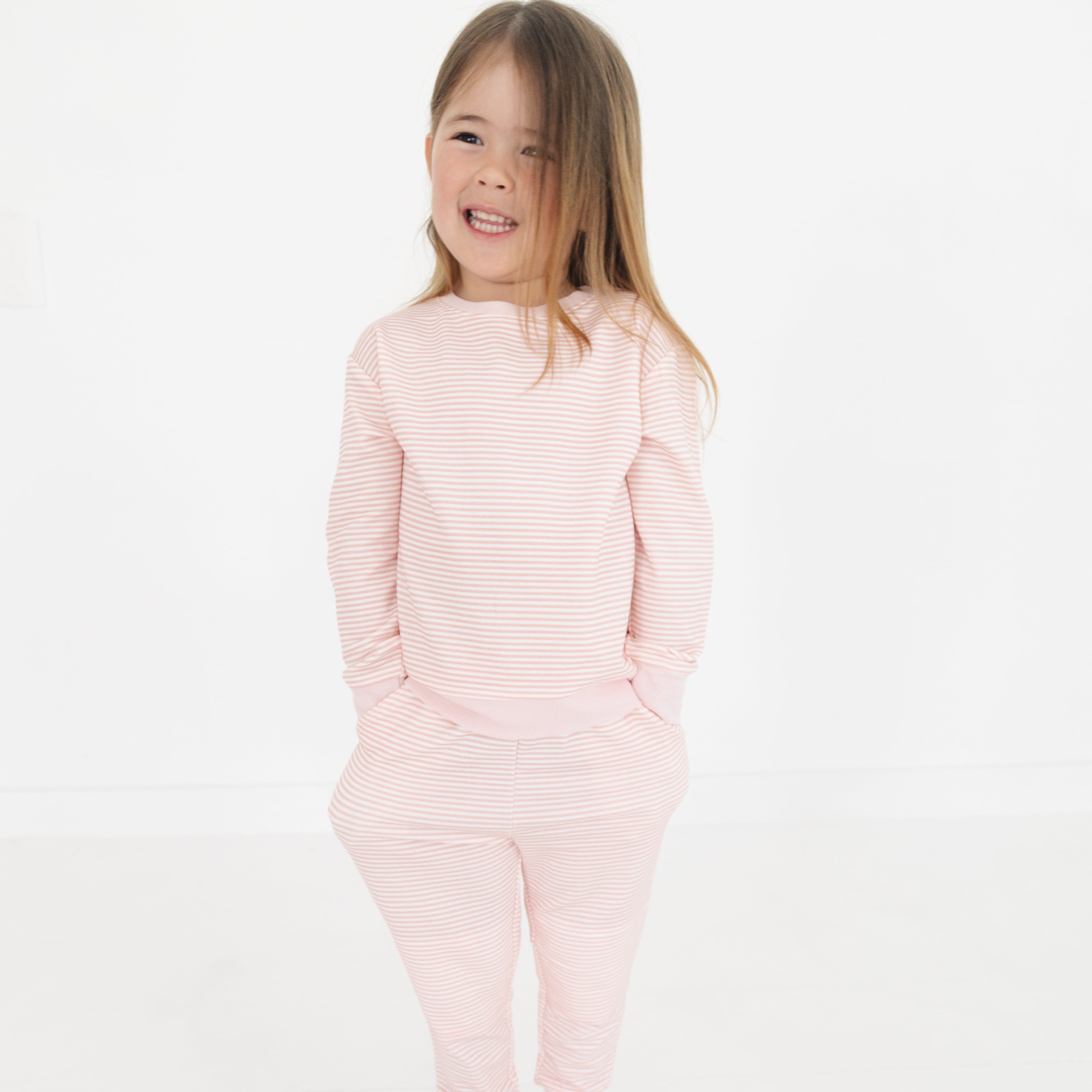 Girl standing with hands in her pockets wearing Motette’s pink striped bamboo sweatsuit, smiling confidently