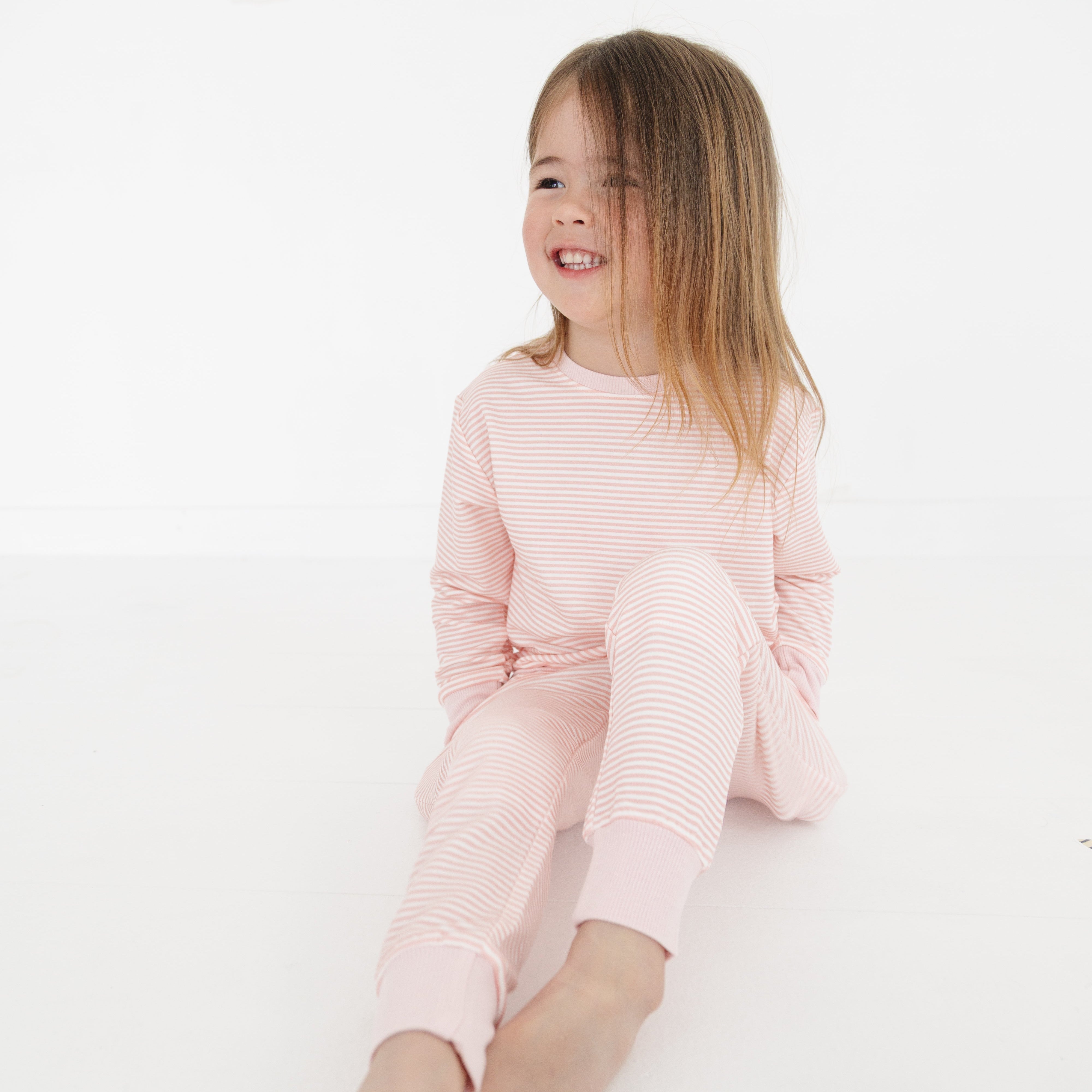 Girl sitting with legs outstretched in the pink striped sweatsuit, looking cozy and playful