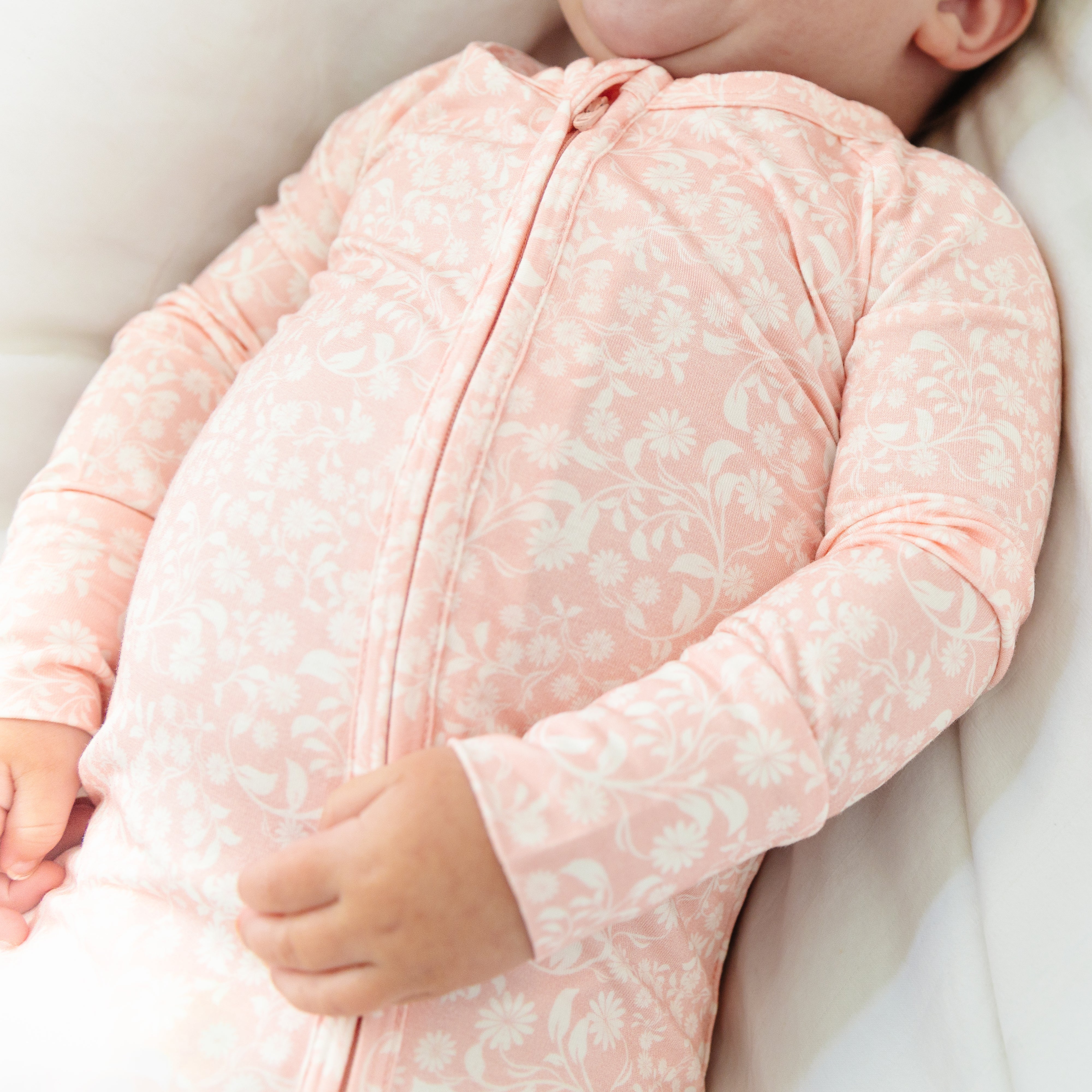 Girl laying down on a bed in Motette’s pink floral bamboo sleeper, looking cozy and relaxed