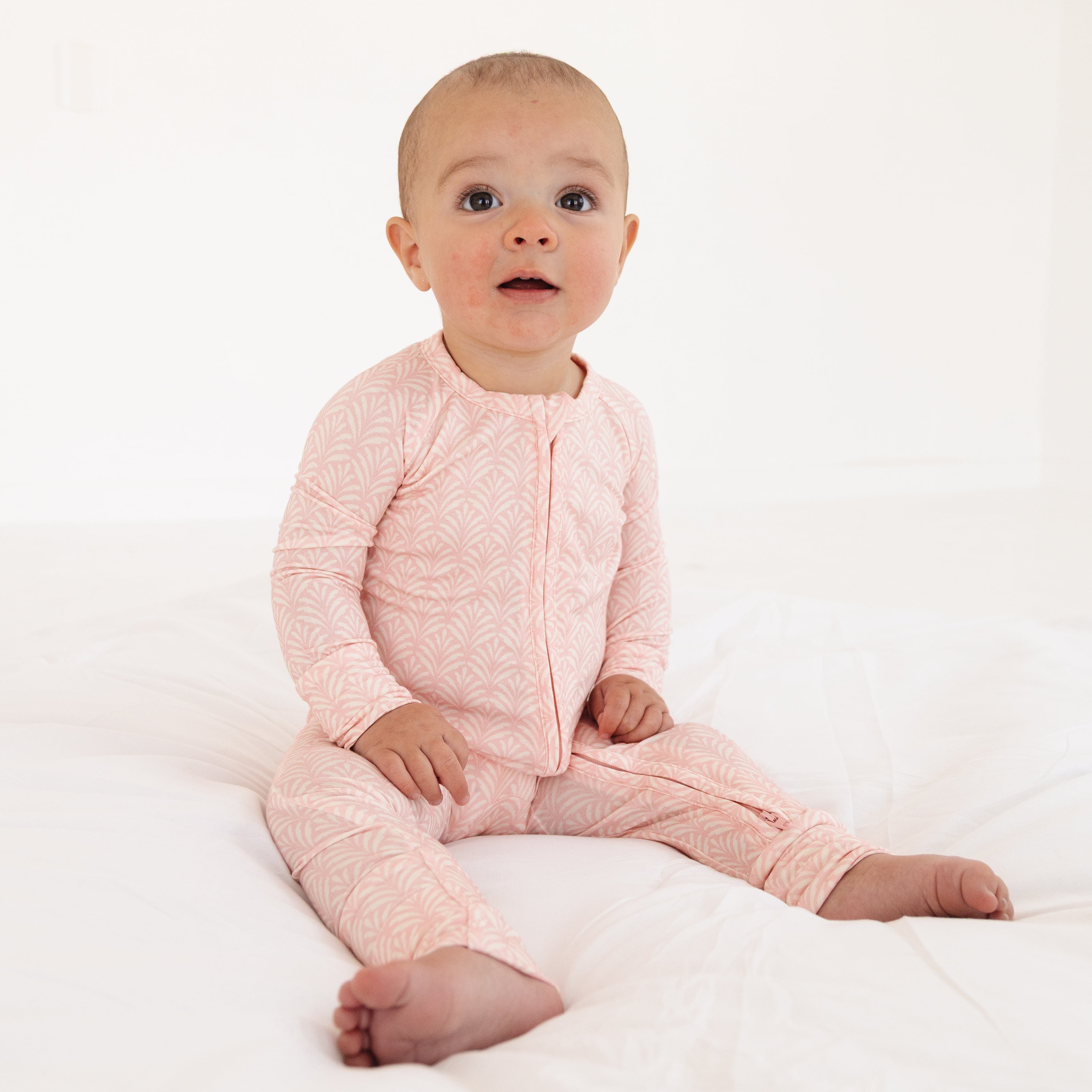 Baby girl sitting up in Motette’s large pink floral bamboo sleeper, featuring pink leaf print with delicate pink and white detailing