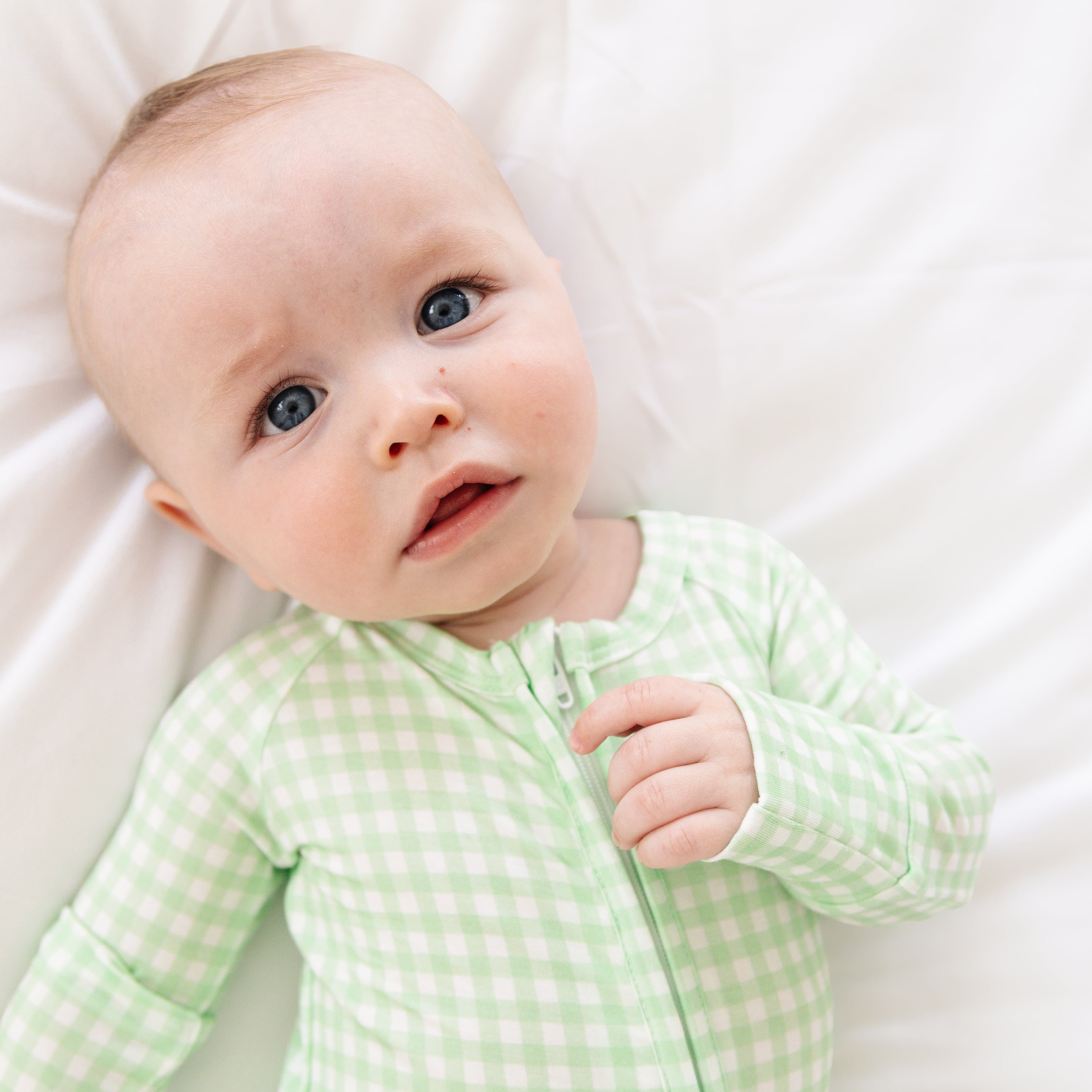 Close up view of baby laying down in the top rated green checkered sleeper, highlighting the relaxed fit and clean checkered design