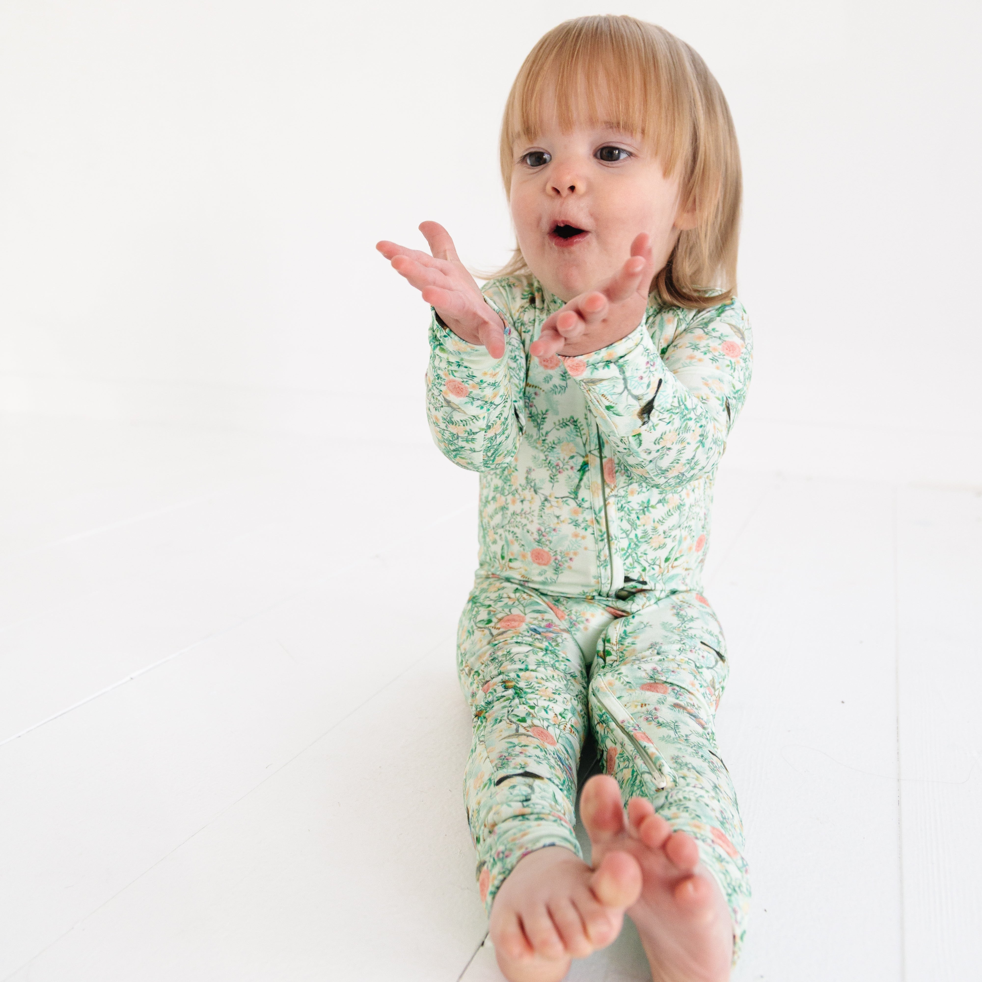 Baby girl wearing green floral bamboo sleeper, smiling while sitting 