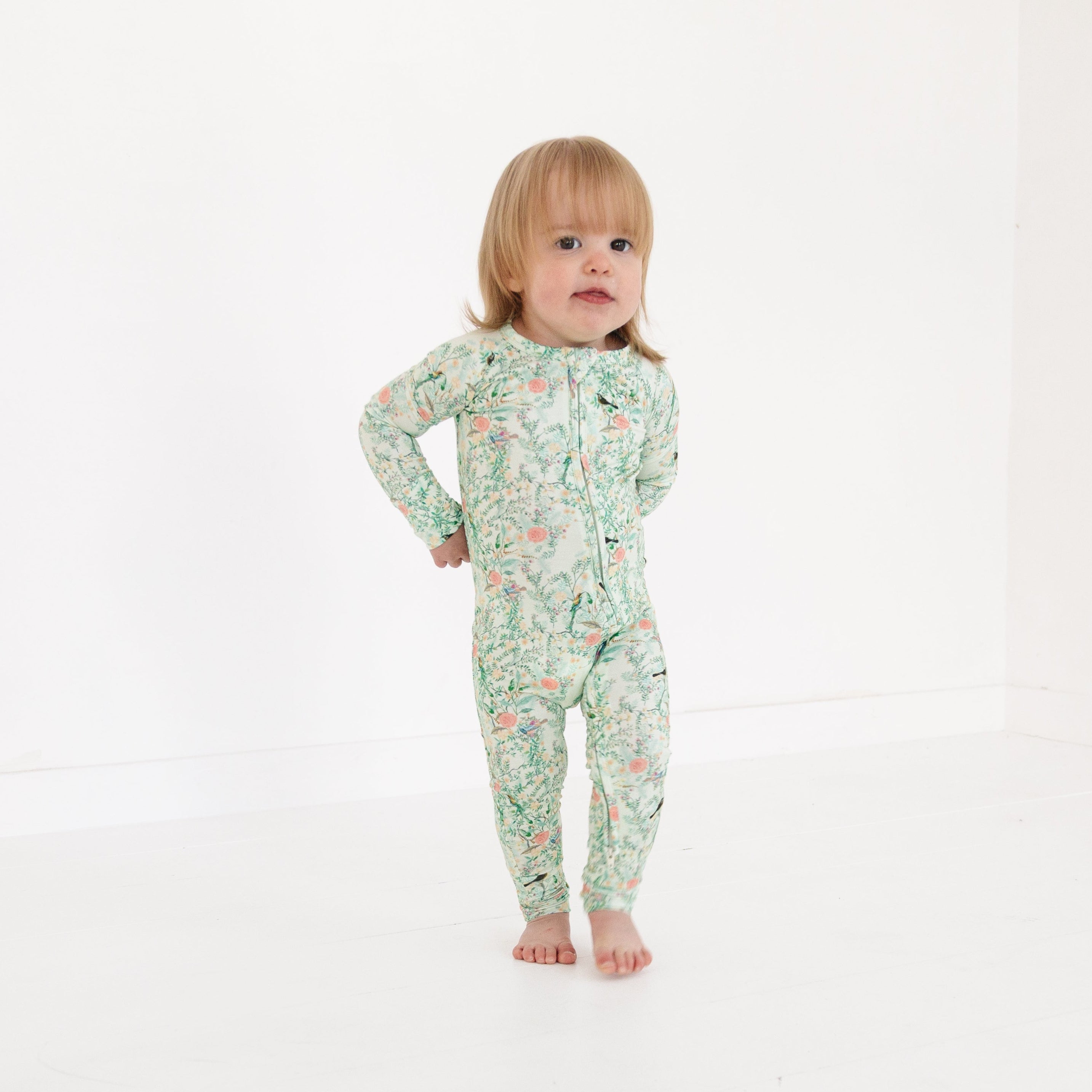 Baby girl lounging in green floral bamboo romper, featuring fold-over cuffs and tag-free neckline.