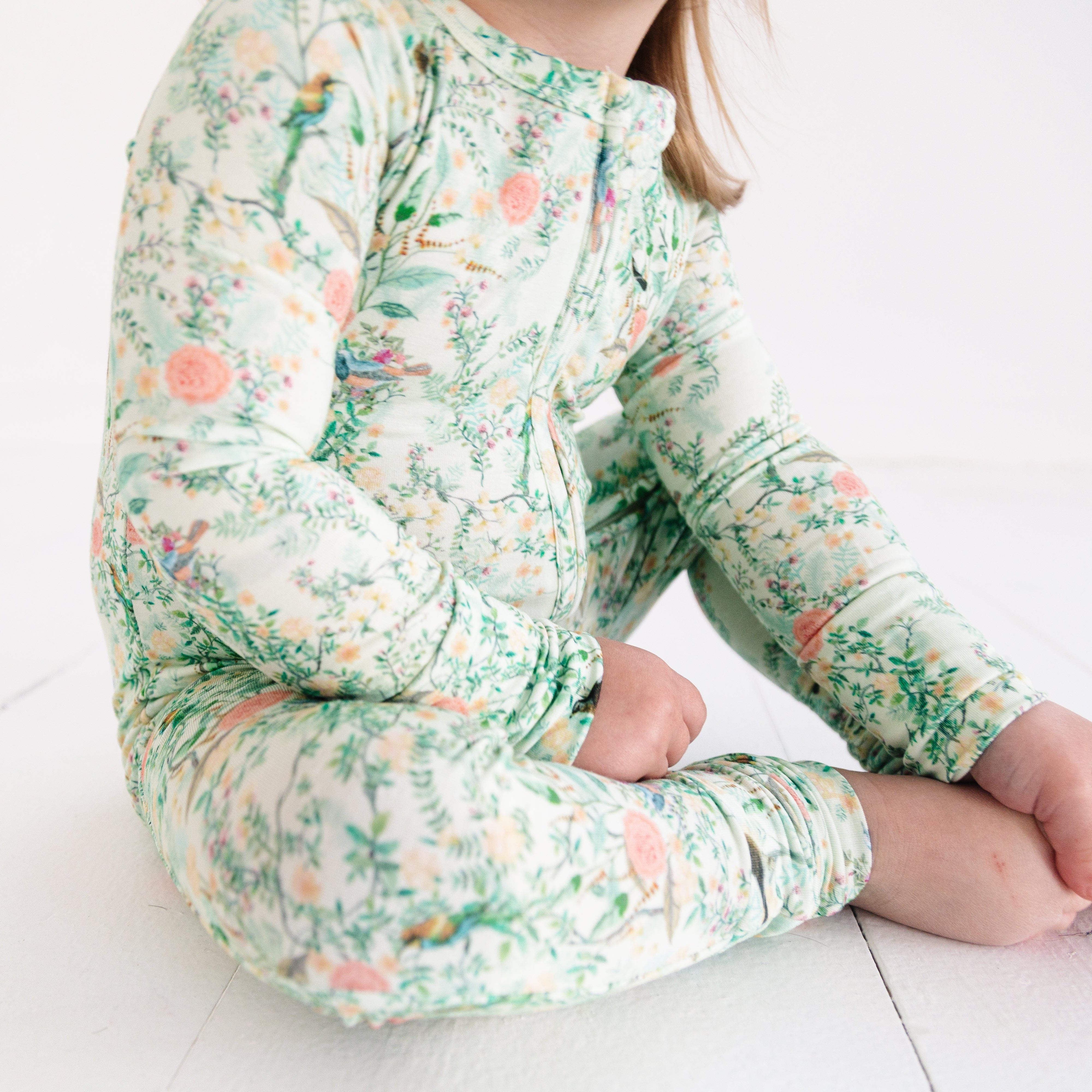 Close-up of baby girl in bamboo sleeper with green floral print, showing two-way zipper and cozy fit.