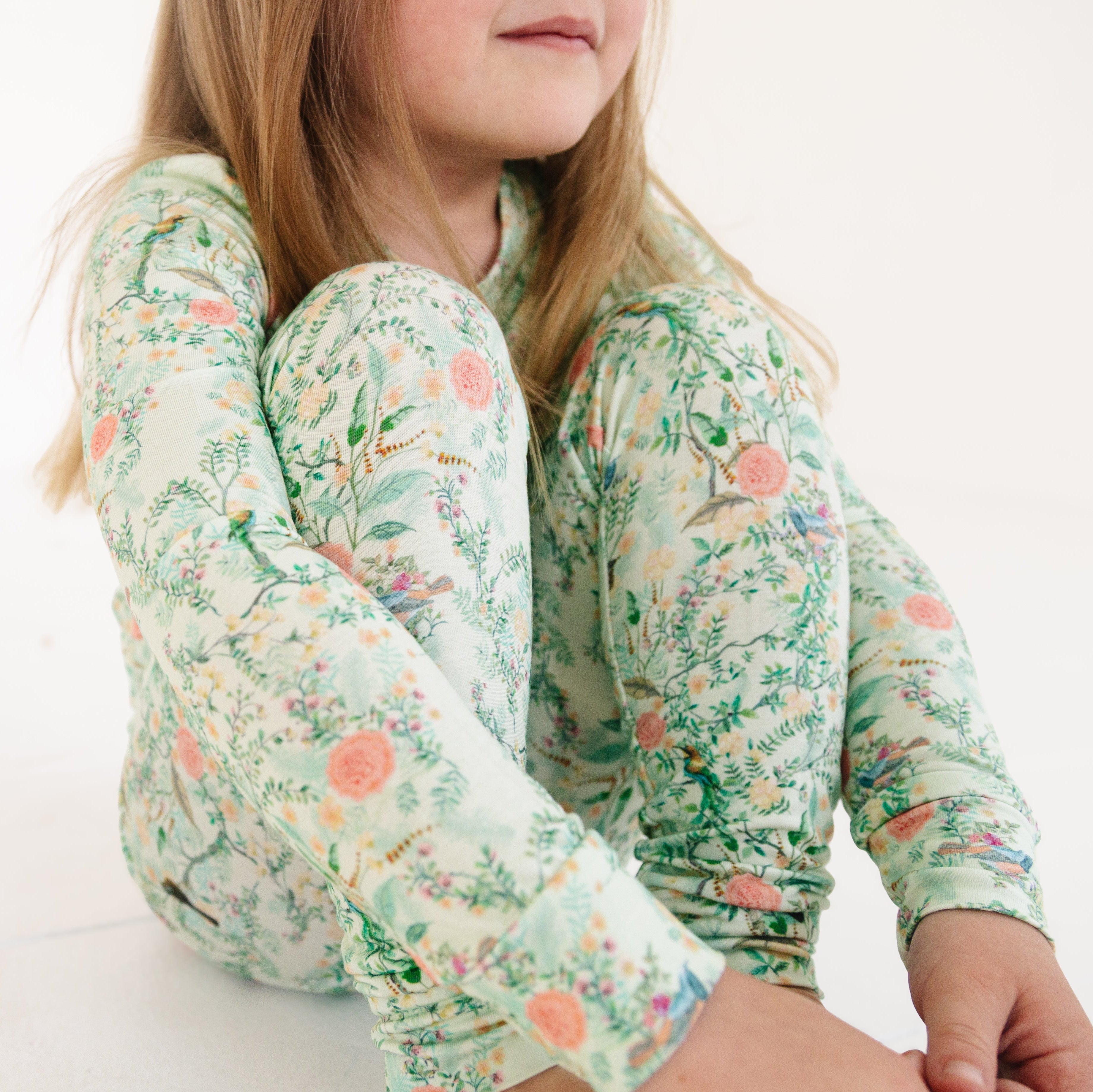 Green floral bamboo pajama set on toddler girl, sitting comfortably on a soft surface.