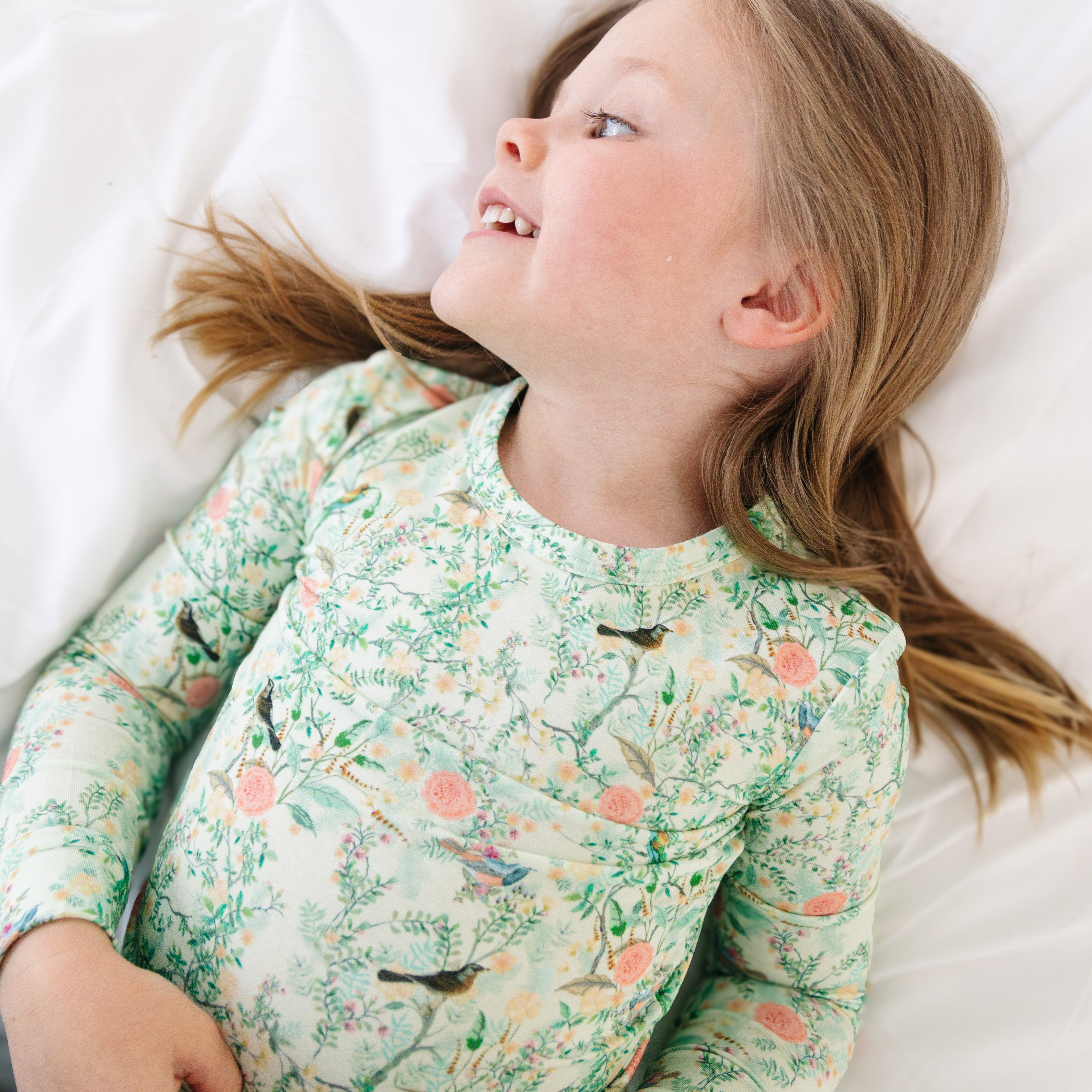 Toddler girl lying down in green floral two-piece bamboo pajamas, relaxed and cozy.
