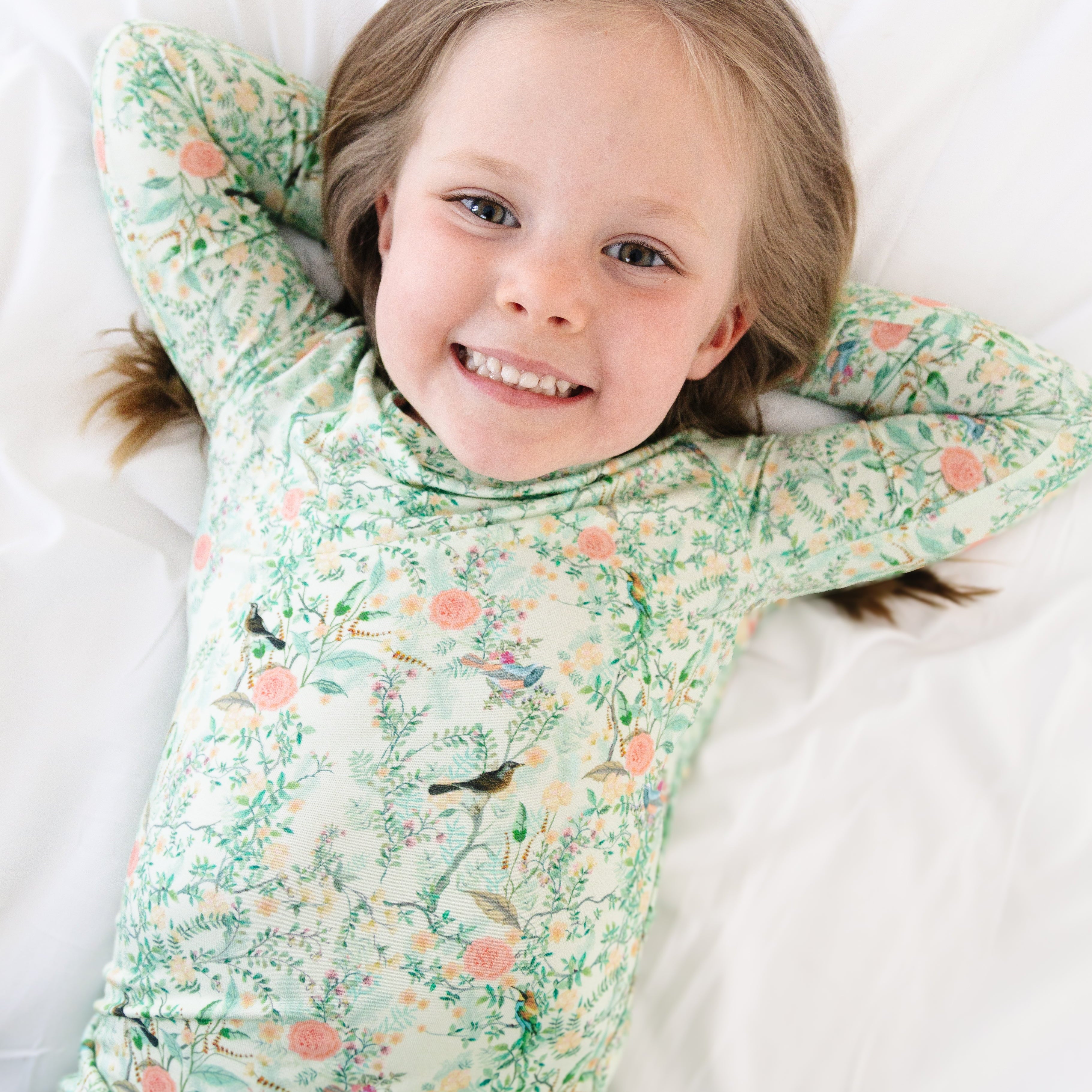 Overhead view of toddler girl laying down in green floral bamboo pajamas, highlighting stretch and softness.